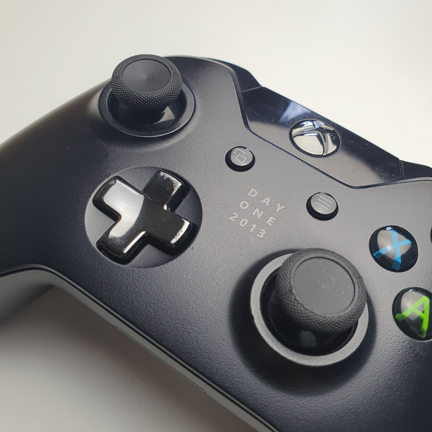 Close-up of a Xbox One controller with 'Day One 2013' visible on a light grey background