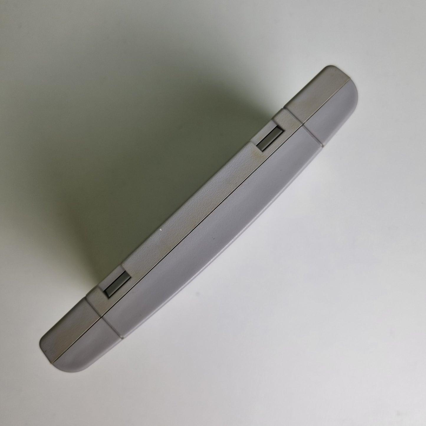 Top view of a Super Nintendo game cartridge showing discolouration between the two sides, on a light grey background