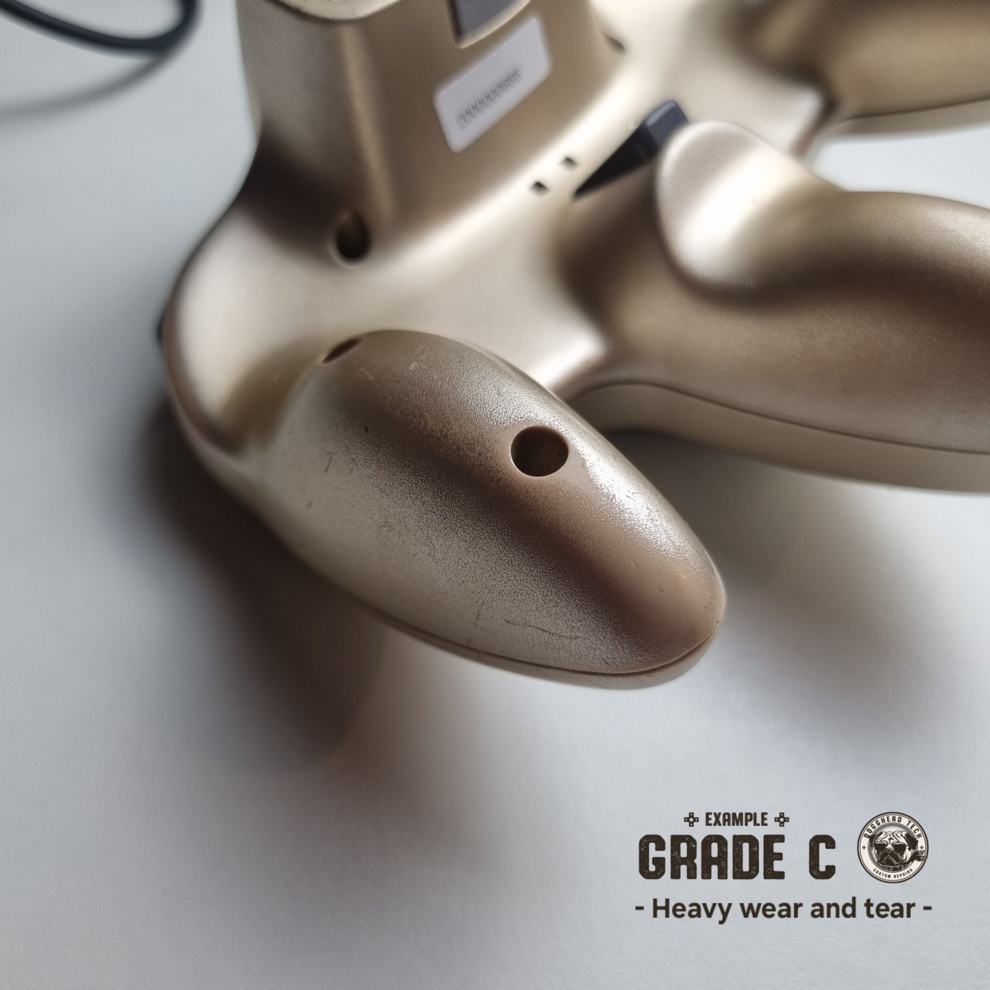 Close-up of the back part of a refurbished modified gold Nintendo 64 controller, showing significant wear and tear. The text reads 'Example Grade C: Heavy wear and tear'.