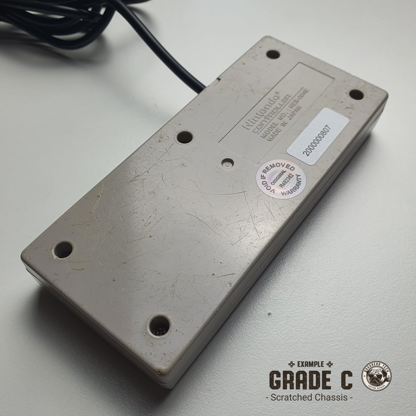 The back of a Nintendo NES controller showing many scratches, pictured on a white background with 'Grade C: Scratched Chassis' text.