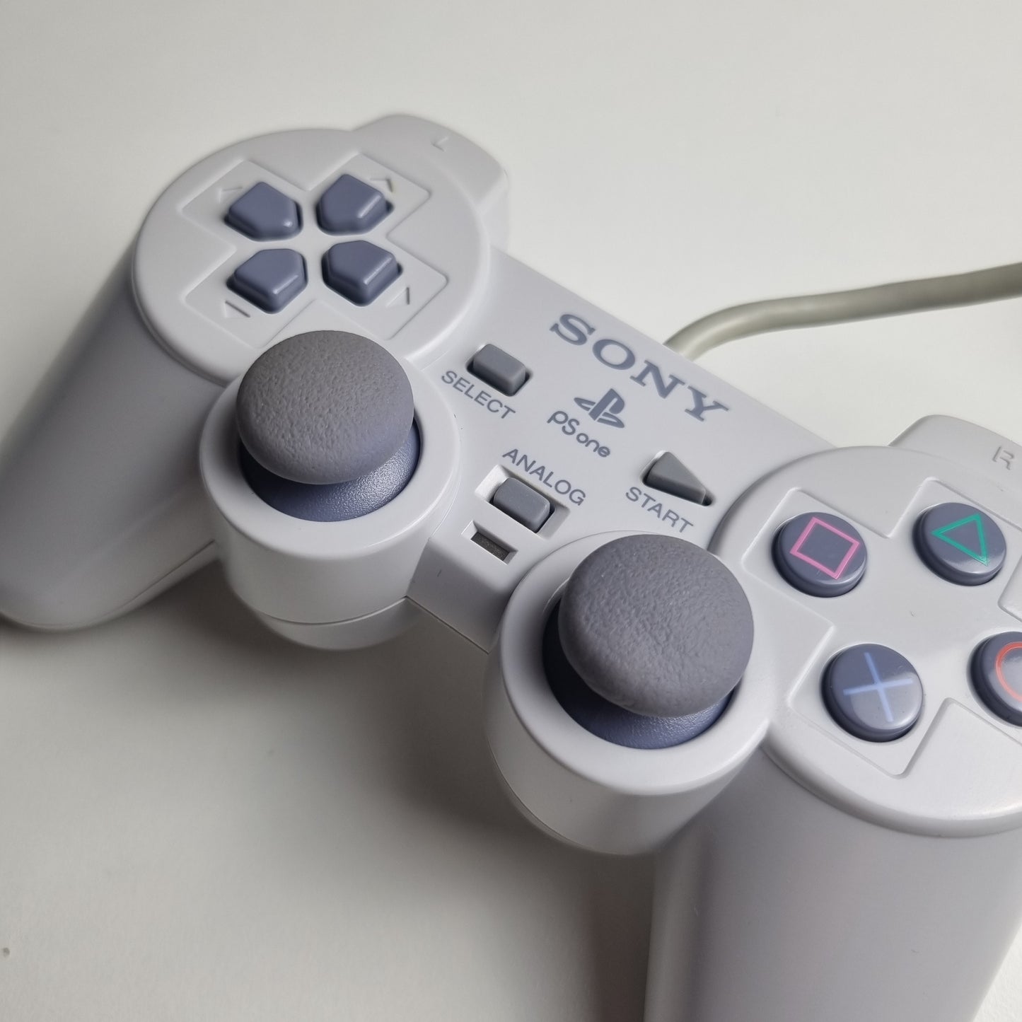 Close-up of a gray official Sony PlayStation 1 refurbished gaming controller on a light gray background