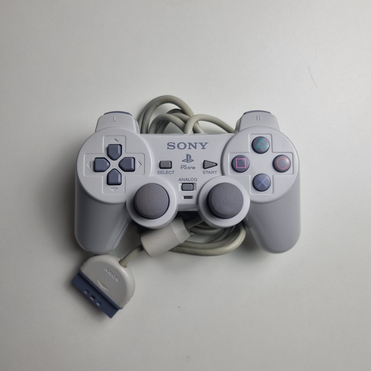 Gray official Sony PlayStation 1  refurbished gaming controller on a light gray background