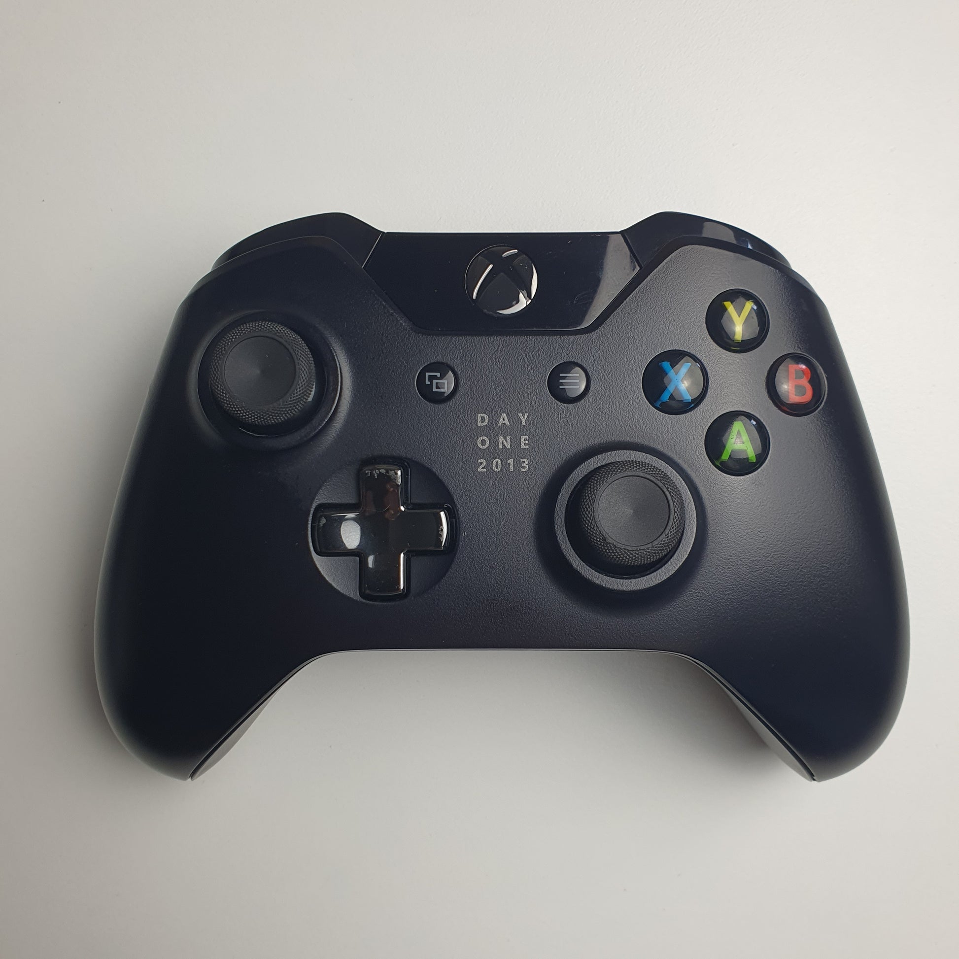 Front of a black 'Day One 2013' Xbox One controller on a white background