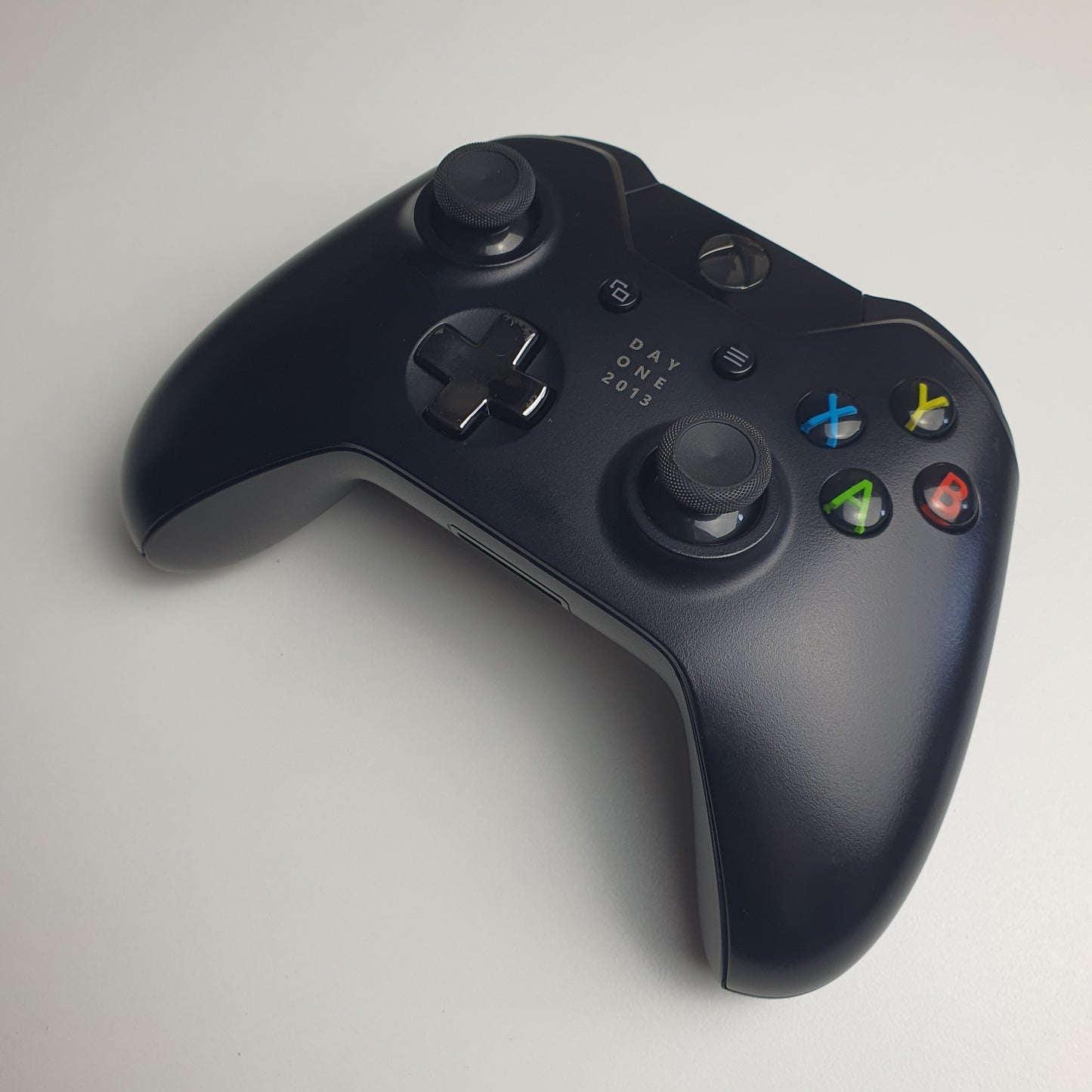 Front of a black 'Day One 2013' Xbox One controller on a white background