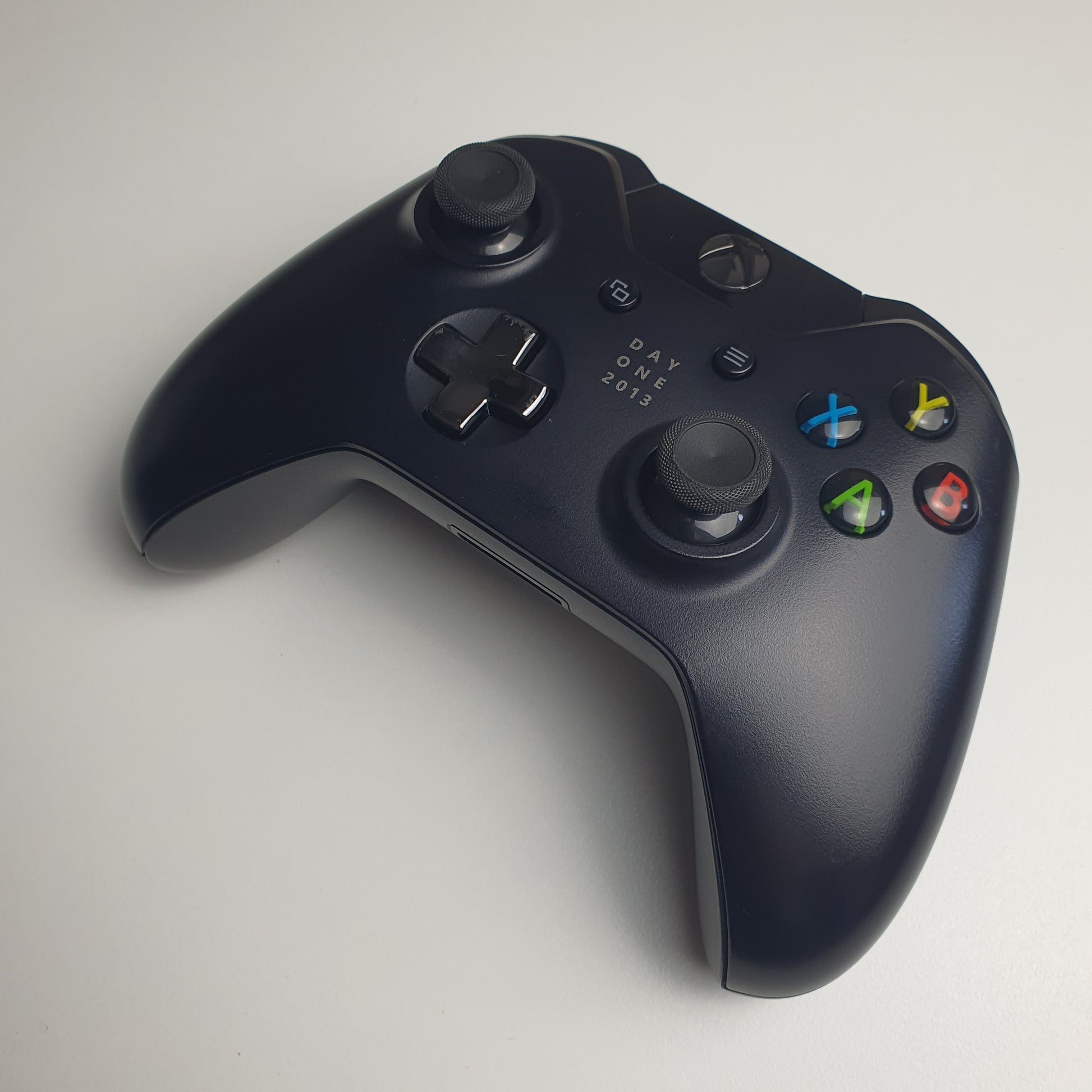 Front of a black 'Day One 2013' Xbox One controller on a white background