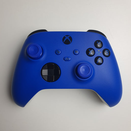 Front of a 'Shock Blue' Xbox game controller showing the front panel, including dual analog sticks, black directional and action buttons, and the Xbox logo, on a light white background.