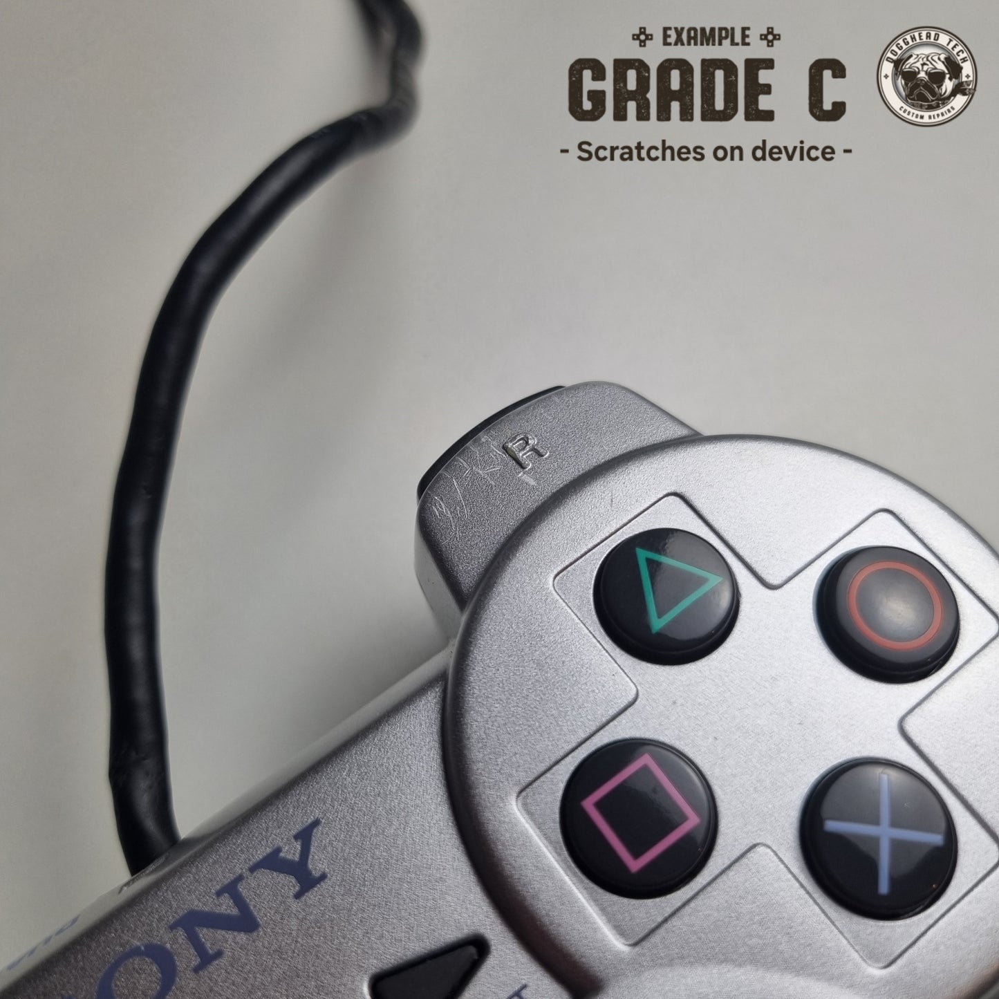 Close-up of some scratches on a refurbished official silver Sony PlayStation 2 wired controller, with the caption 'Grade C: Scratches on device' in the top corner.
