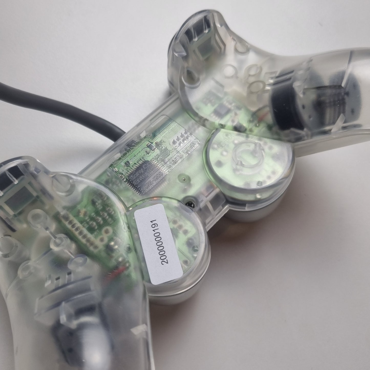 Close-up of a clear official Sony PlayStation 1 refurbished gaming controller with buttons on a white background