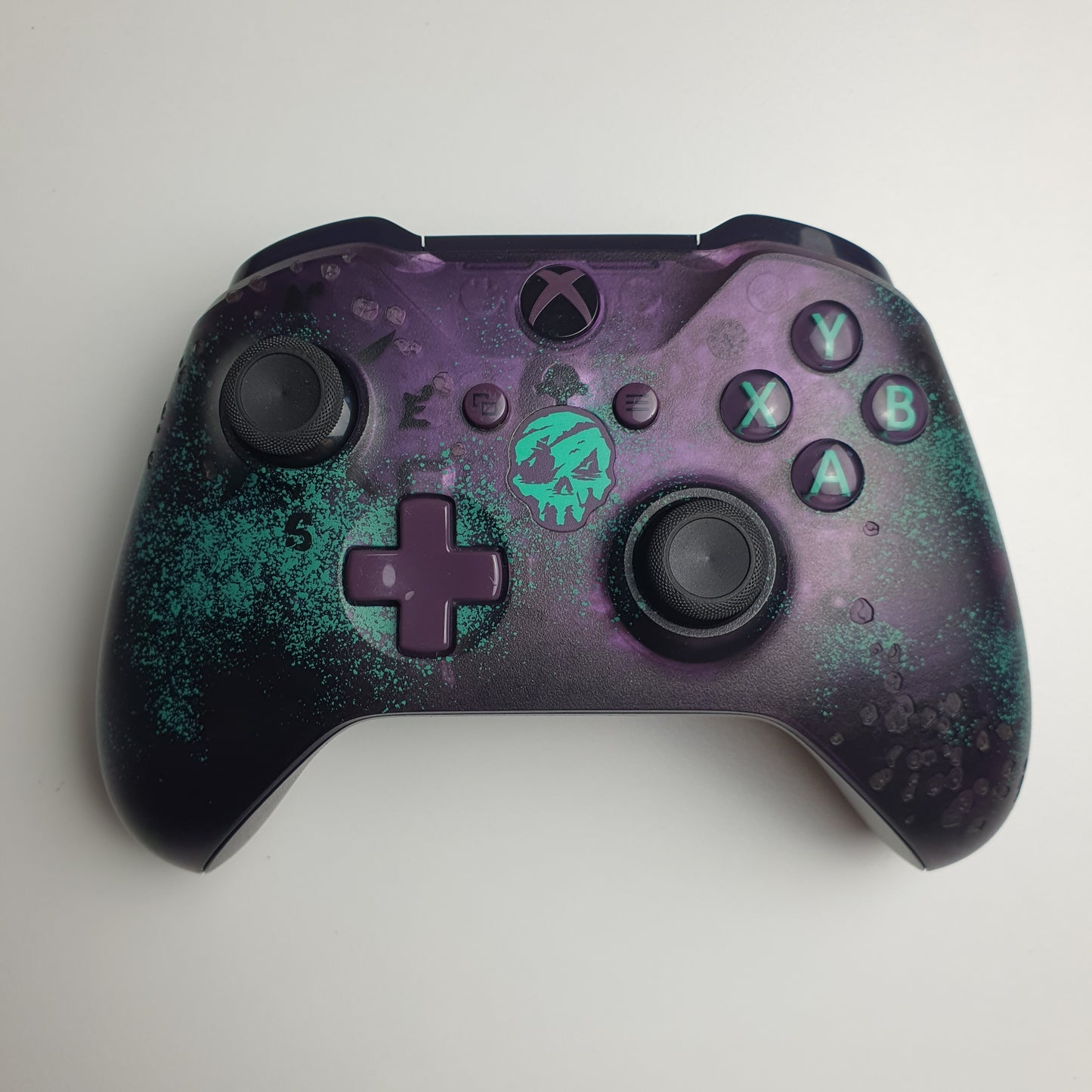 Front of a turquoise & purple Xbox One 'Sea of Thieves' controller on a white background
