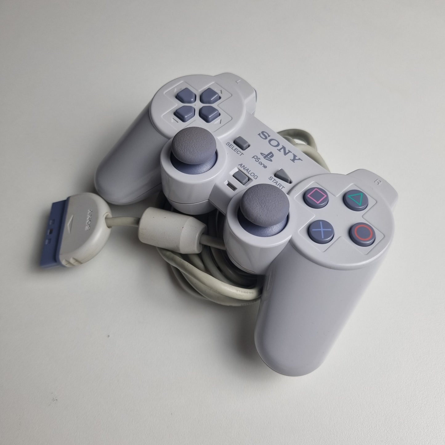 Gray official Sony PlayStation 1  refurbished gaming controller on a light gray background
