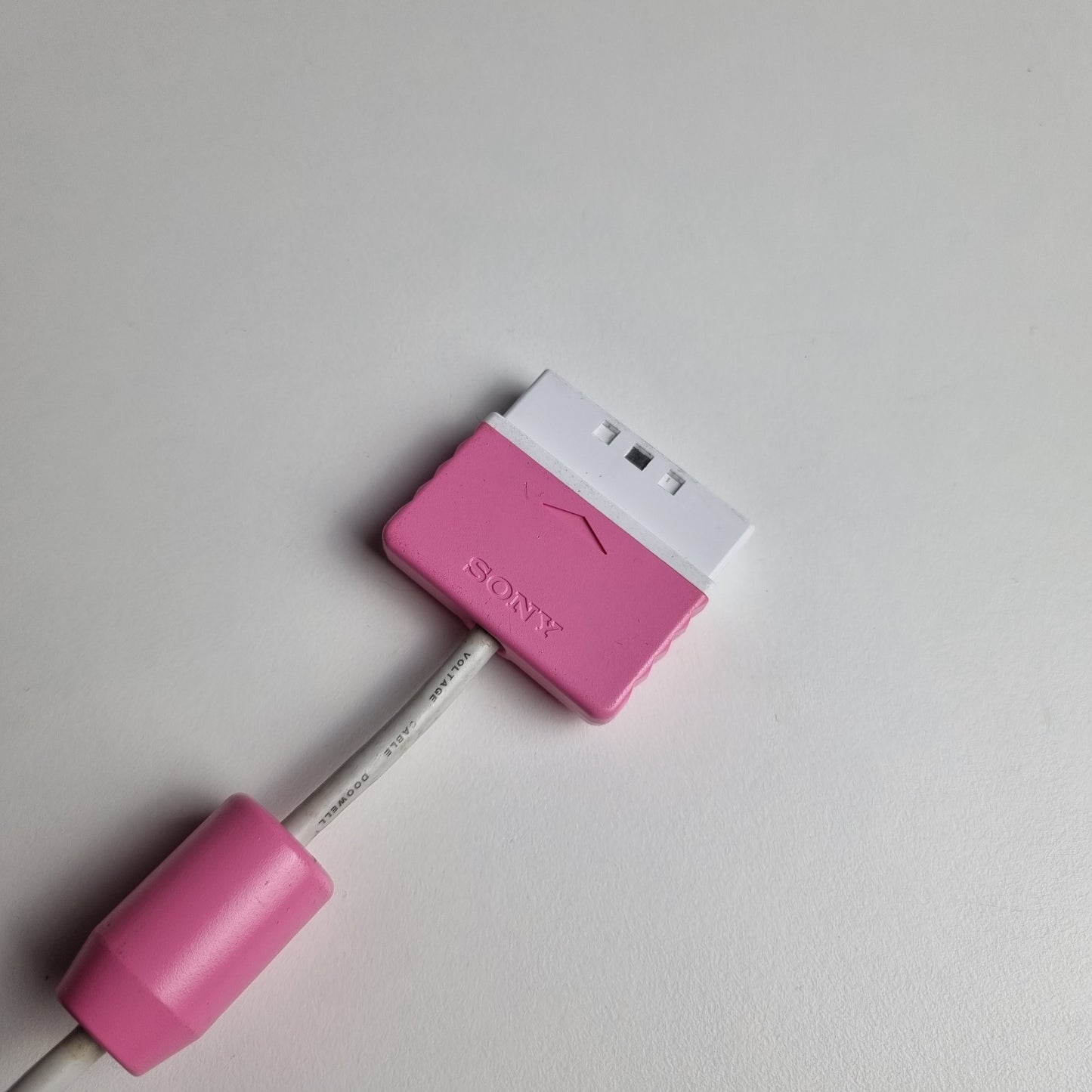 Cable and connector of an official Sony PlayStation 2 DualShock refurbished pink wired controller on a light gray background