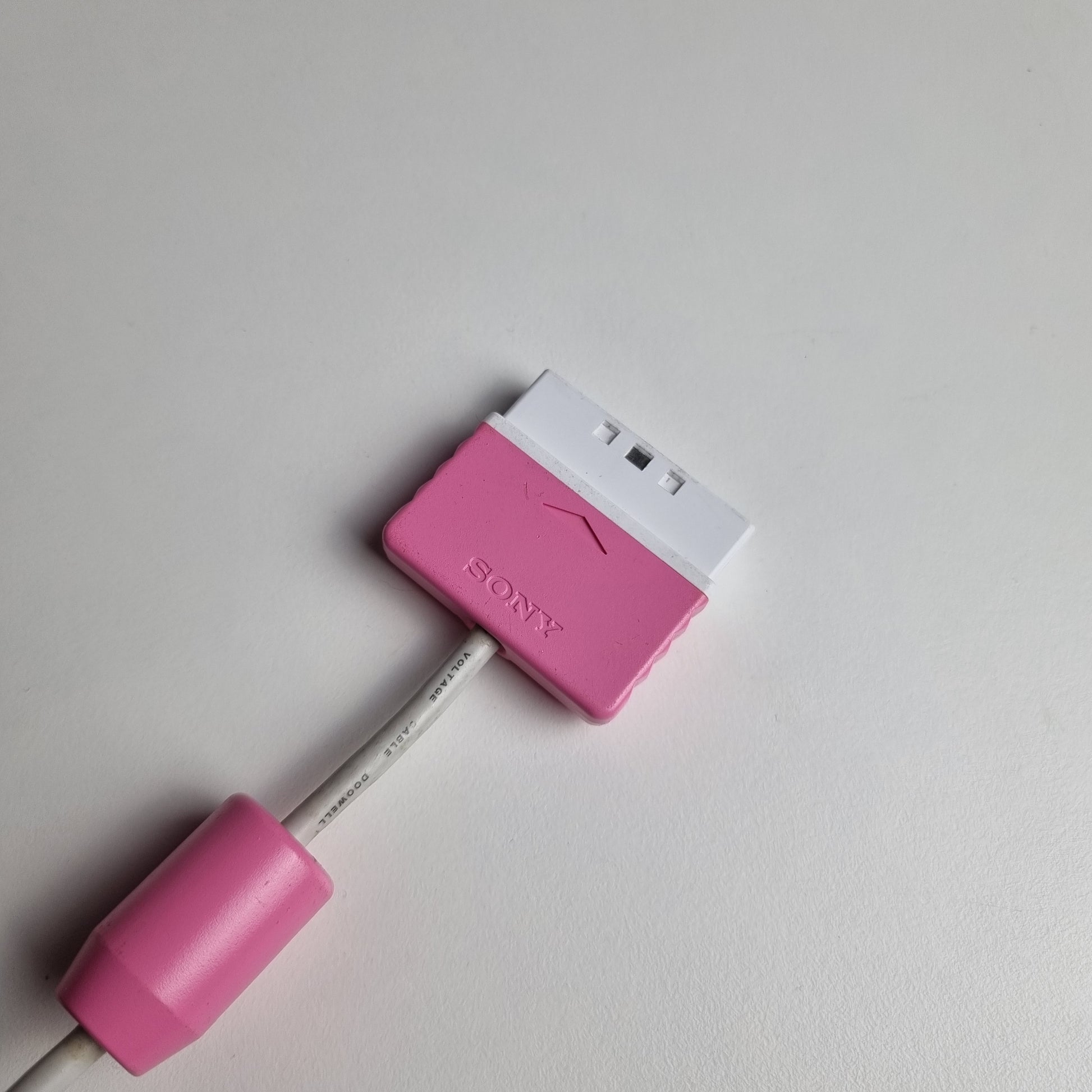 Cable and connector of an official Sony PlayStation 2 DualShock refurbished pink wired controller on a light gray background