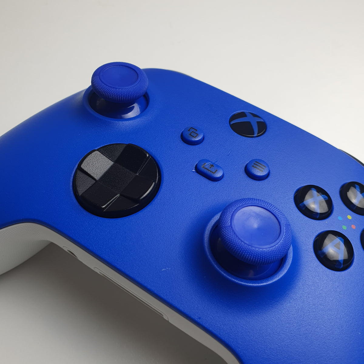 A close-up of a 'Shock Blue' Xbox game controller showing the front panel, including dual analog sticks, black directional and action buttons, and the Xbox logo, on a light white background.