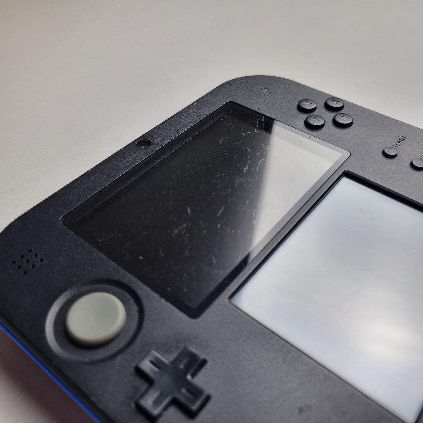 Close-up of a handheld gaming console showing surface scratches with a screen and control buttons on a light grey background