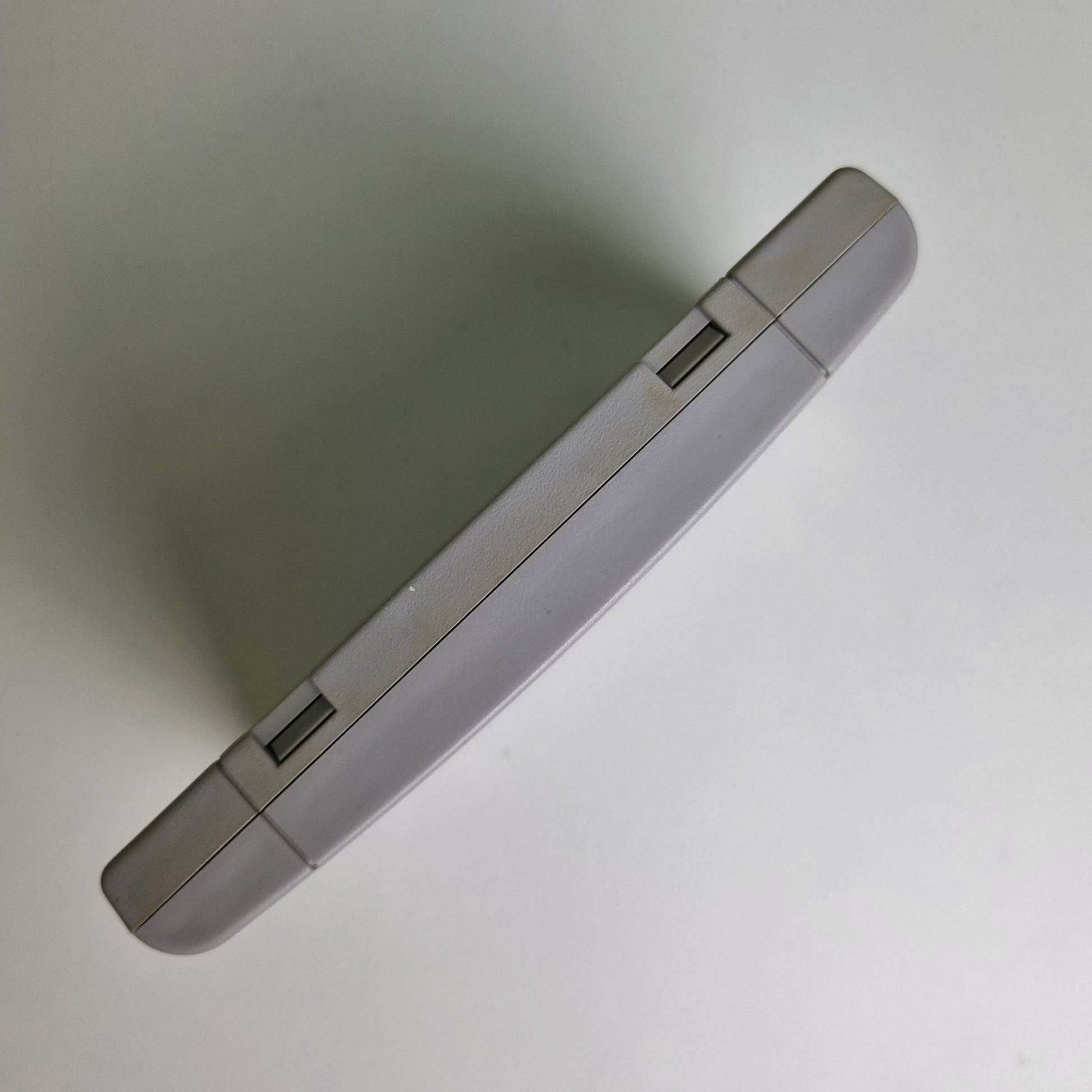 Top view of a Super Nintendo game cartridge showing discolouration between the two sides, on a light grey background