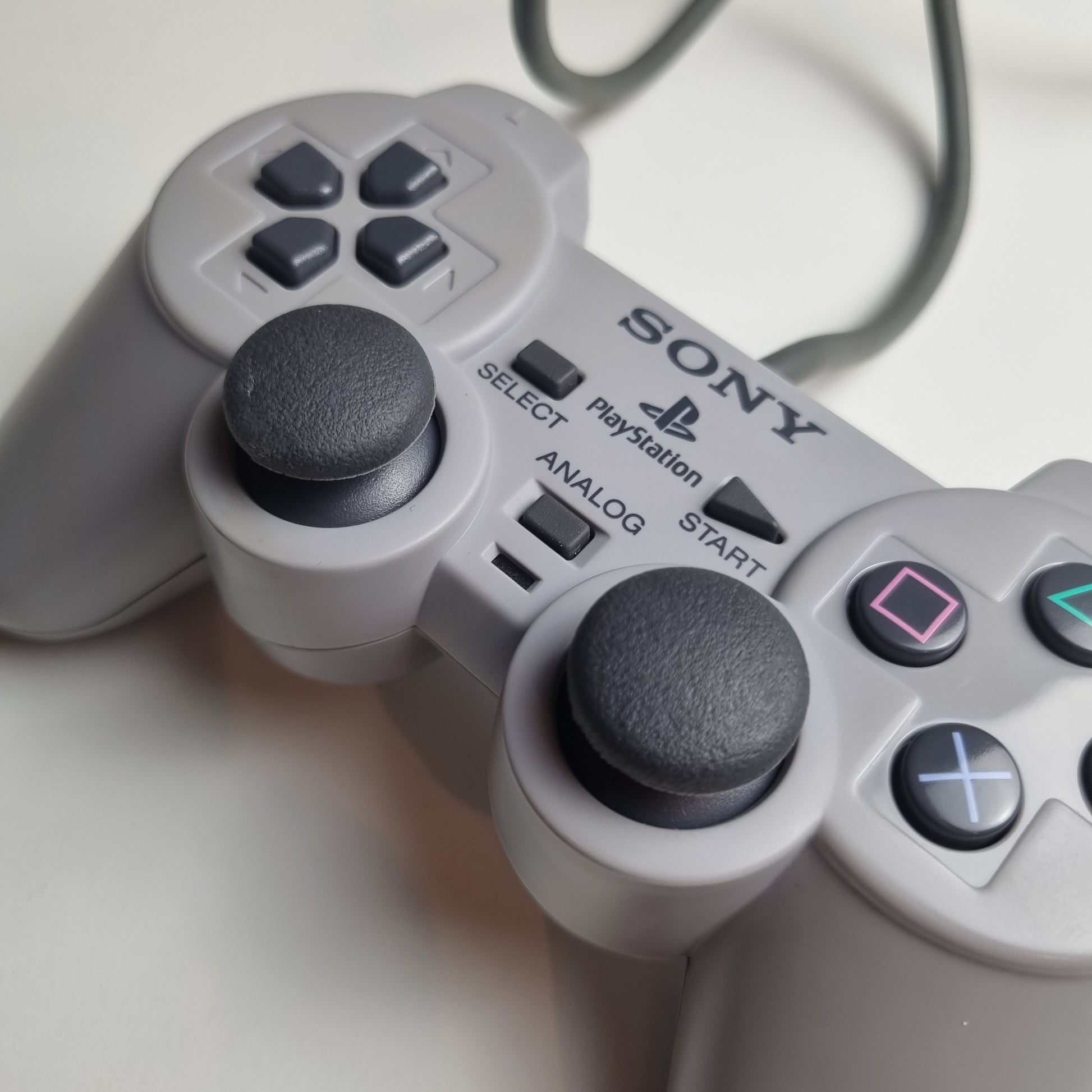 Close-up of the analog sticks on a refurbished official Sony PlayStation DualShock wired grey controller, on a white background.