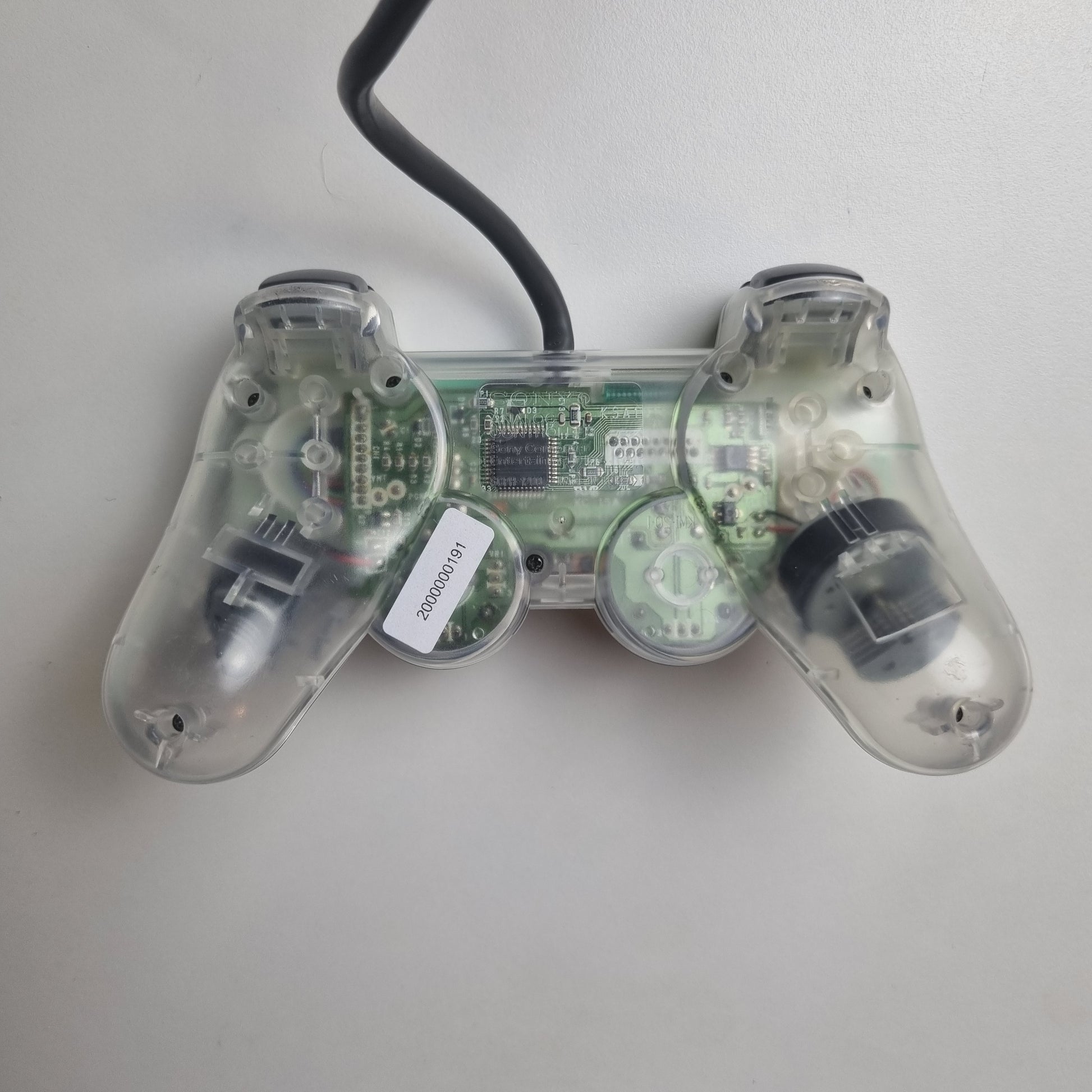 The back of a clear official Sony PlayStation 1 refurbished gaming controller with buttons on a white background