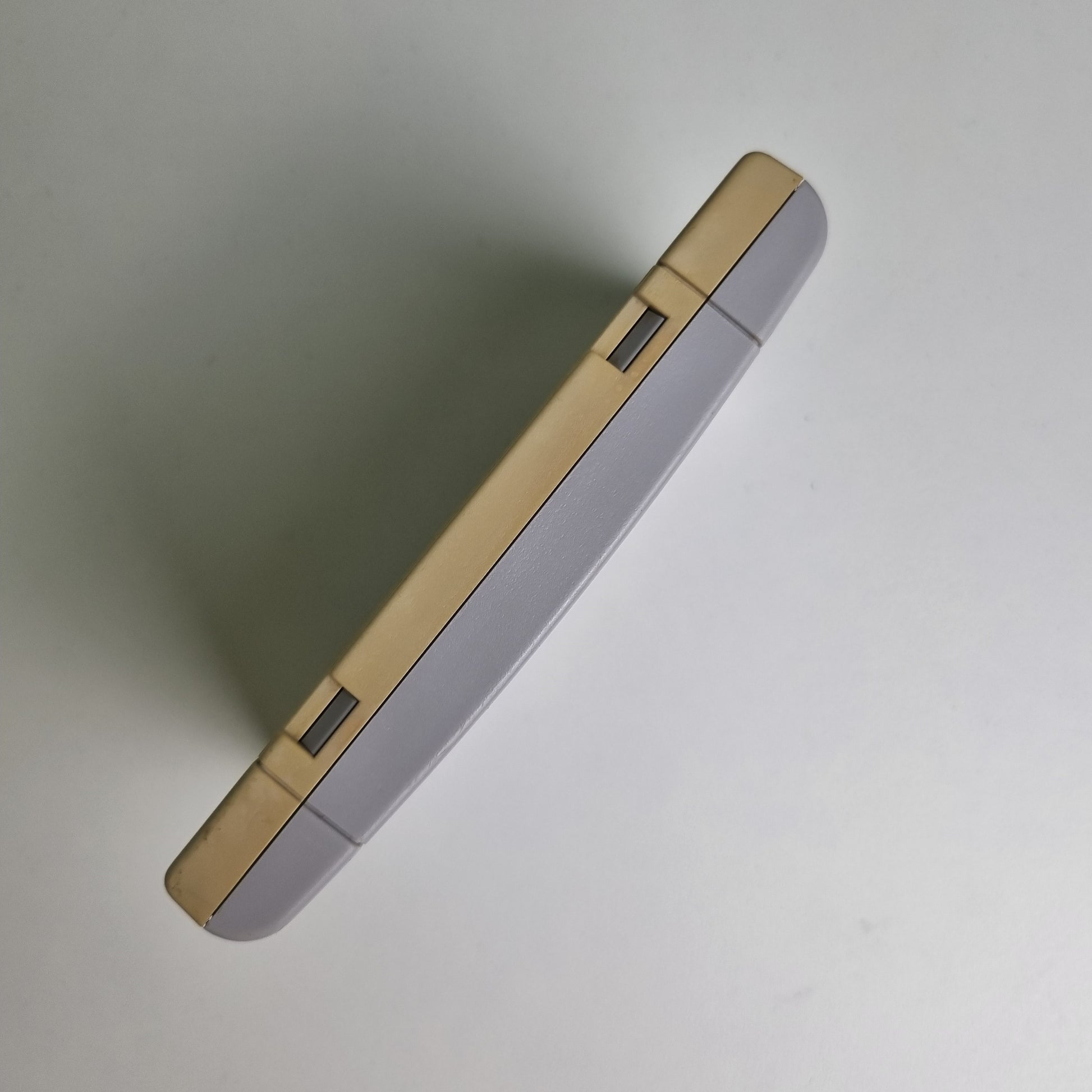 Top view of a Super Nintendo game cartridge showing discolouration between the two sides, on a light grey background