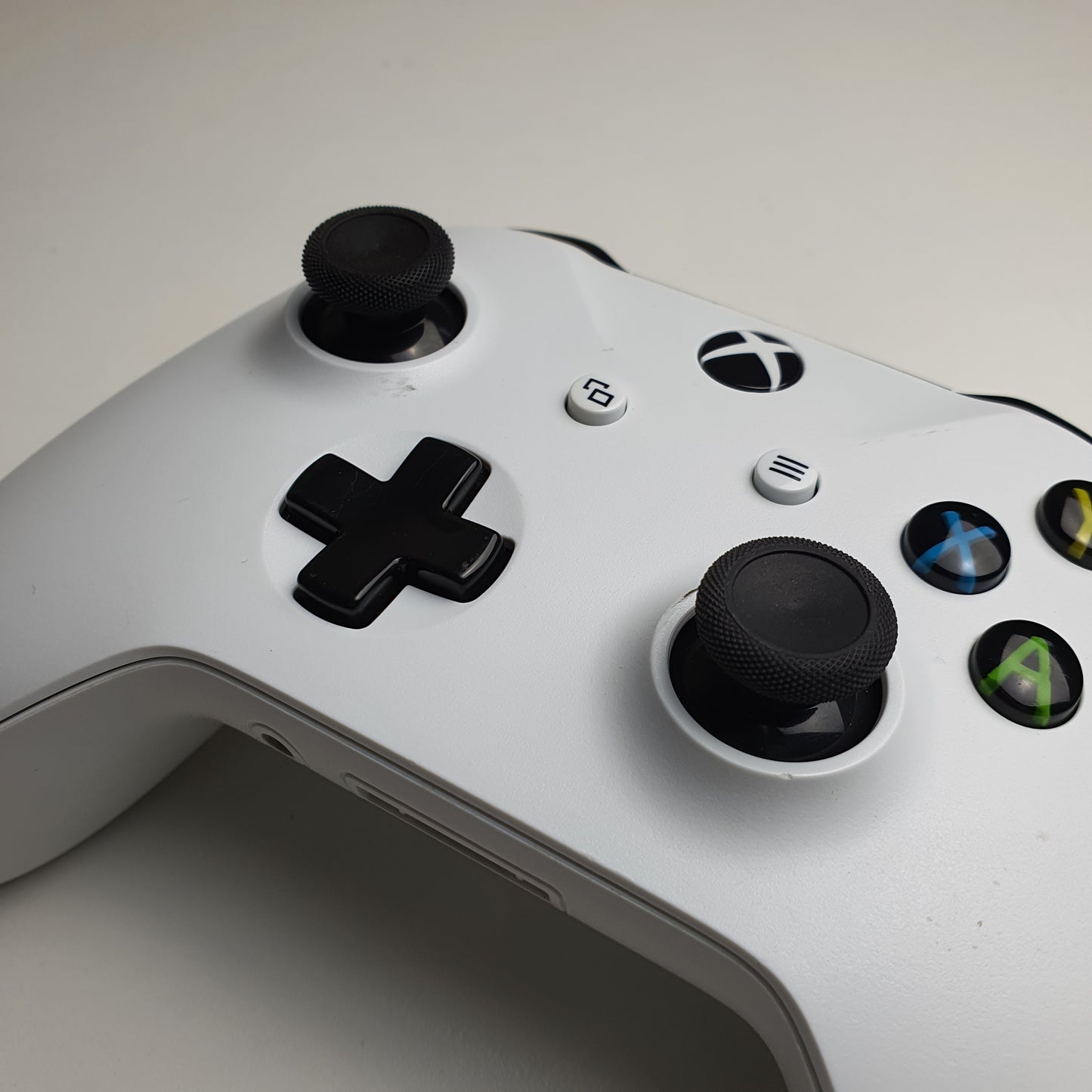 Close-up of a white Xbox One controller with black buttons on a light grey background