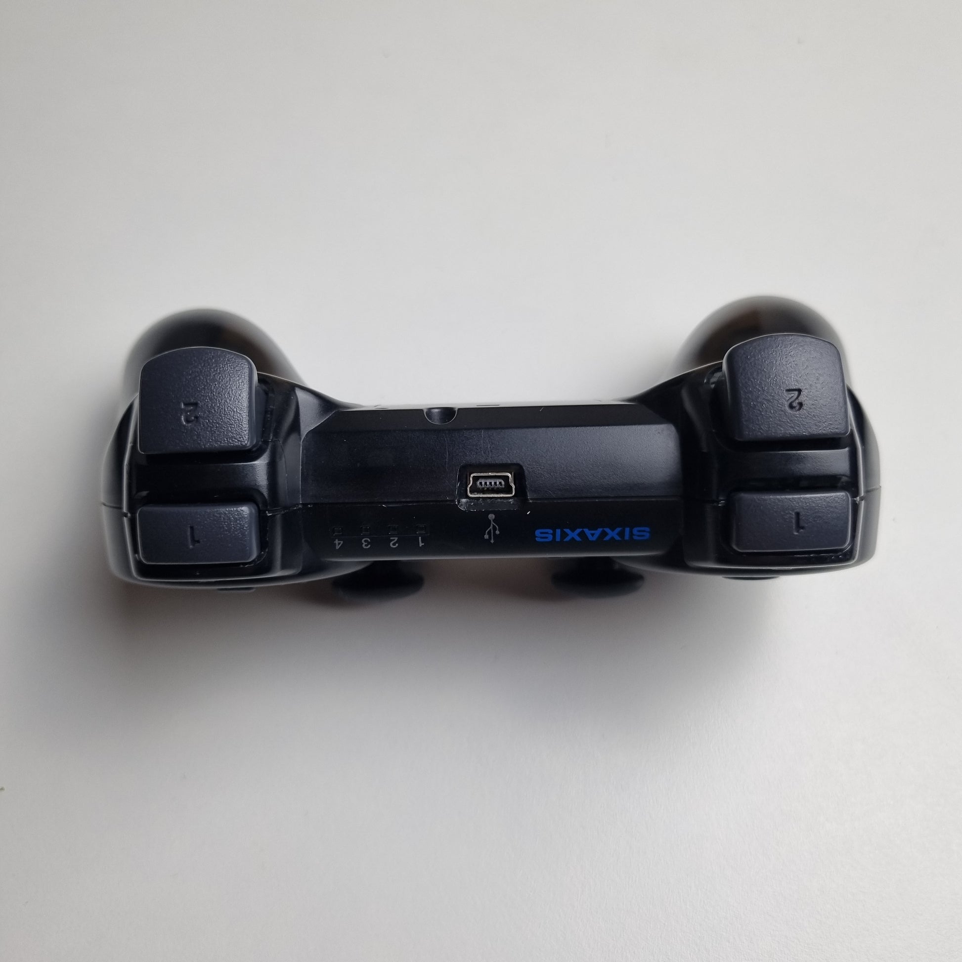 Top of a official Sony PlayStation PS3 SIXAXIS black wireless controller on a white background.