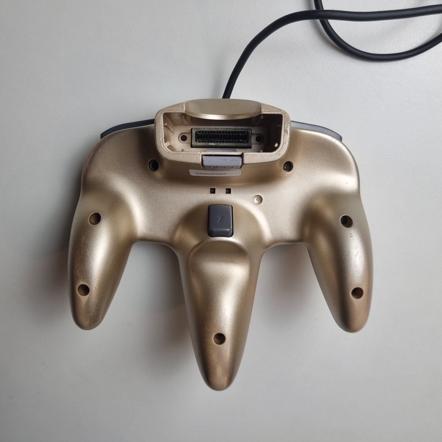 The back of a refurbished modified gold Nintendo 64 controller on a light grey background.