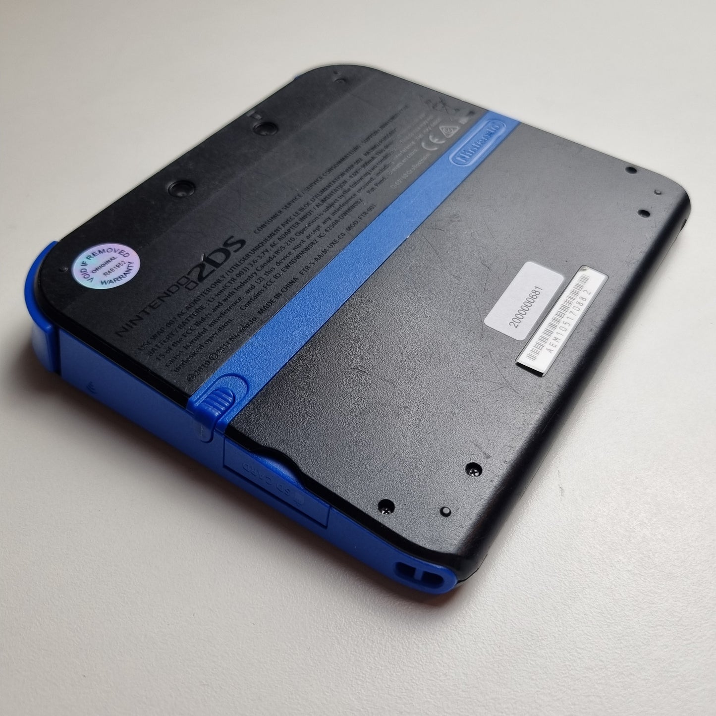 Back of a refurbished Nintendo 2DS black & blue handheld gaming console on a light grey background