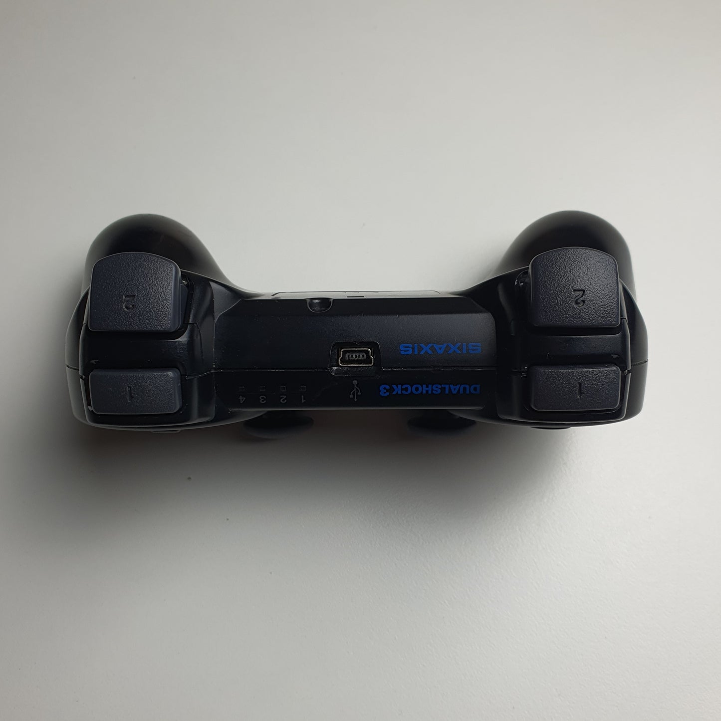 Top of a black PlayStation 3 controller on a white background
