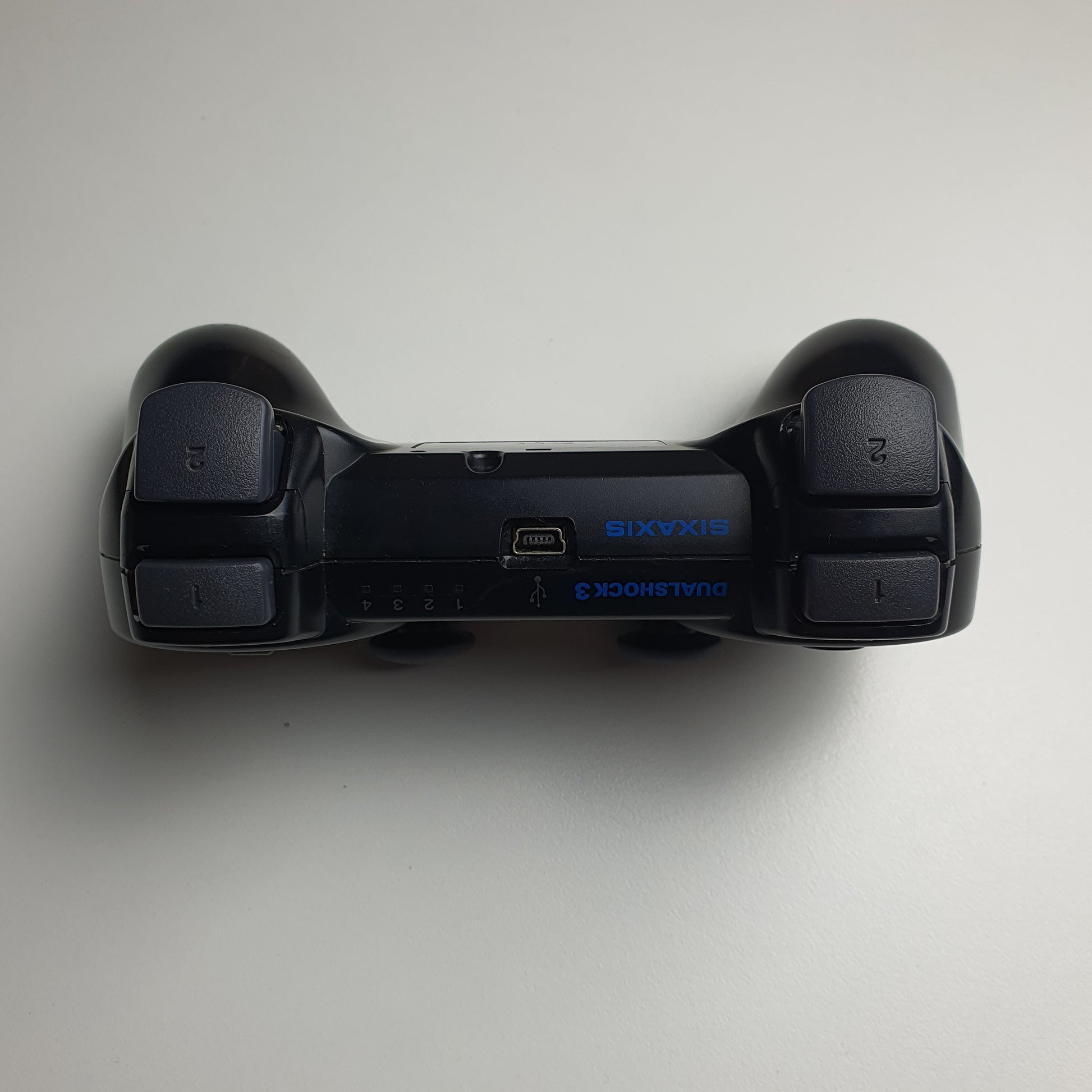 Top of a black PlayStation 3 controller on a white background