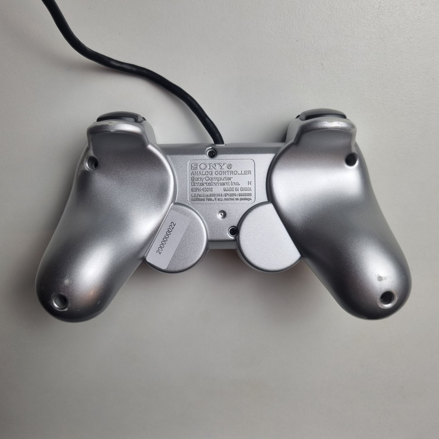 The back of a refurbished official silver Sony PlayStation 2 wired controller, showing signs of wear and tear.