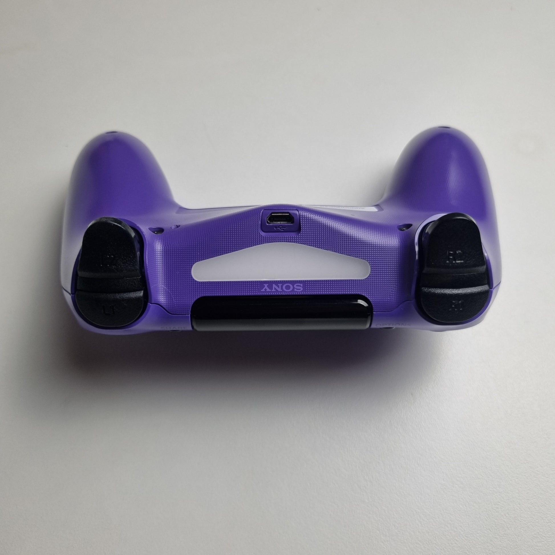 Top of an electric purple official Sony PlayStation DualShock 4 refurbished gaming controller on a light gray background