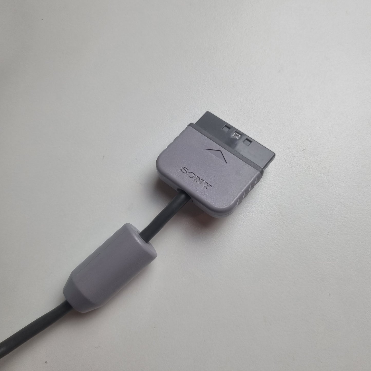 Gray official Sony PlayStation 1 cable with a connector for a refurbished clear gaming controller on a white background