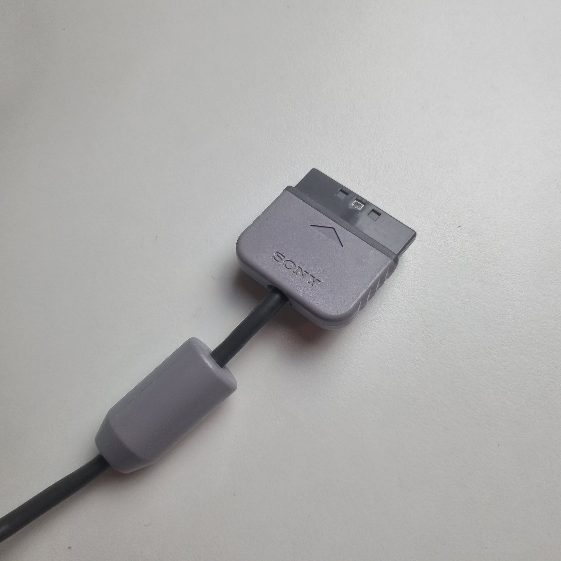 Gray official Sony PlayStation 1 cable with a connector for a refurbished clear gaming controller on a white background