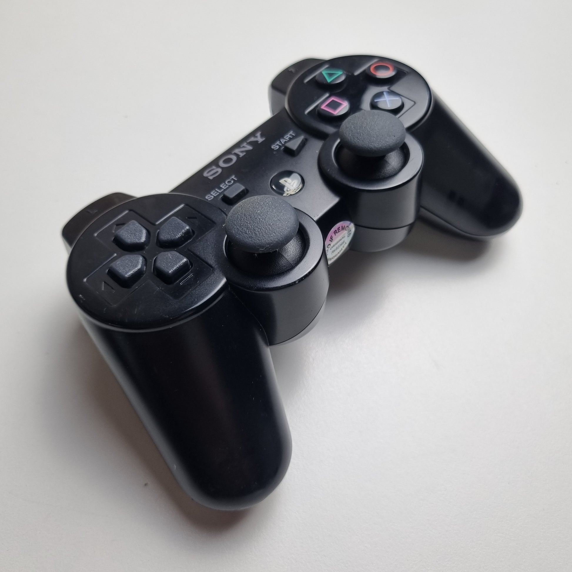 Angled picture of a official Sony PlayStation PS3 SIXAXIS black wireless controller on a white background.
