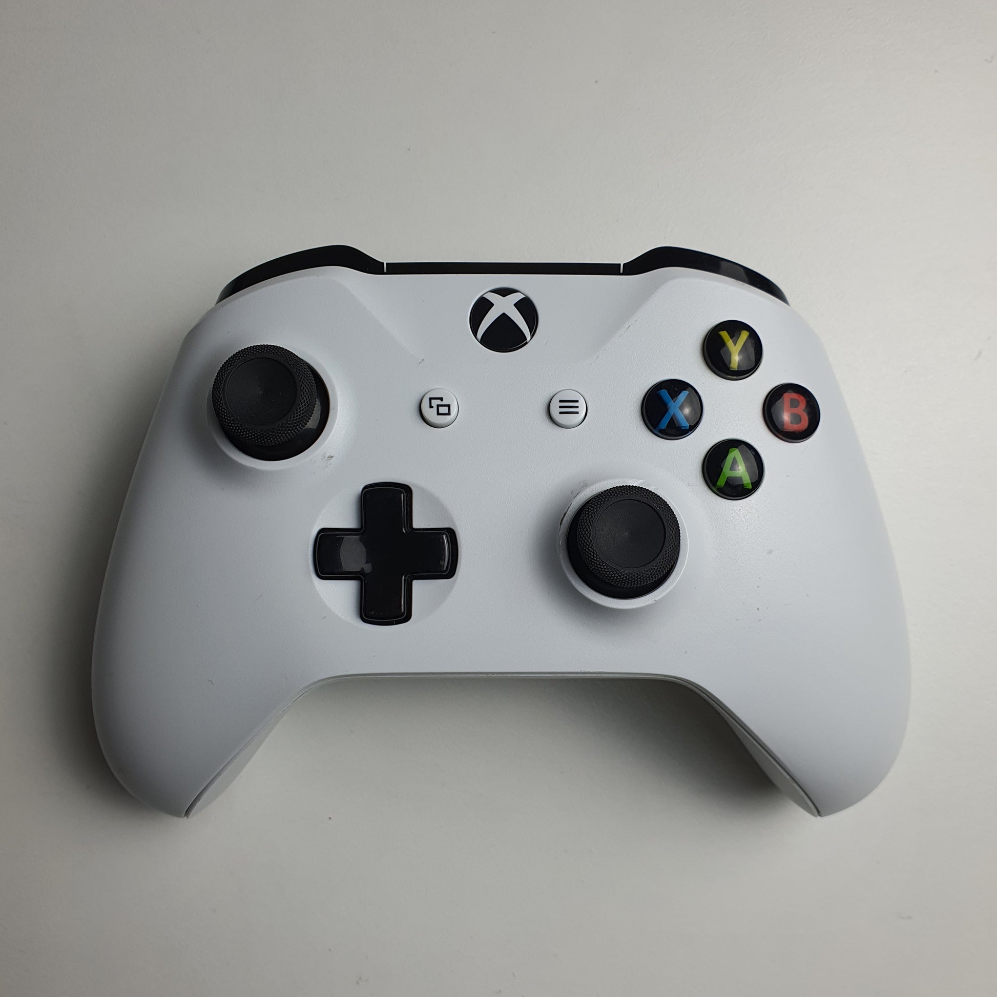A white Xbox One controller with black buttons on a light grey background