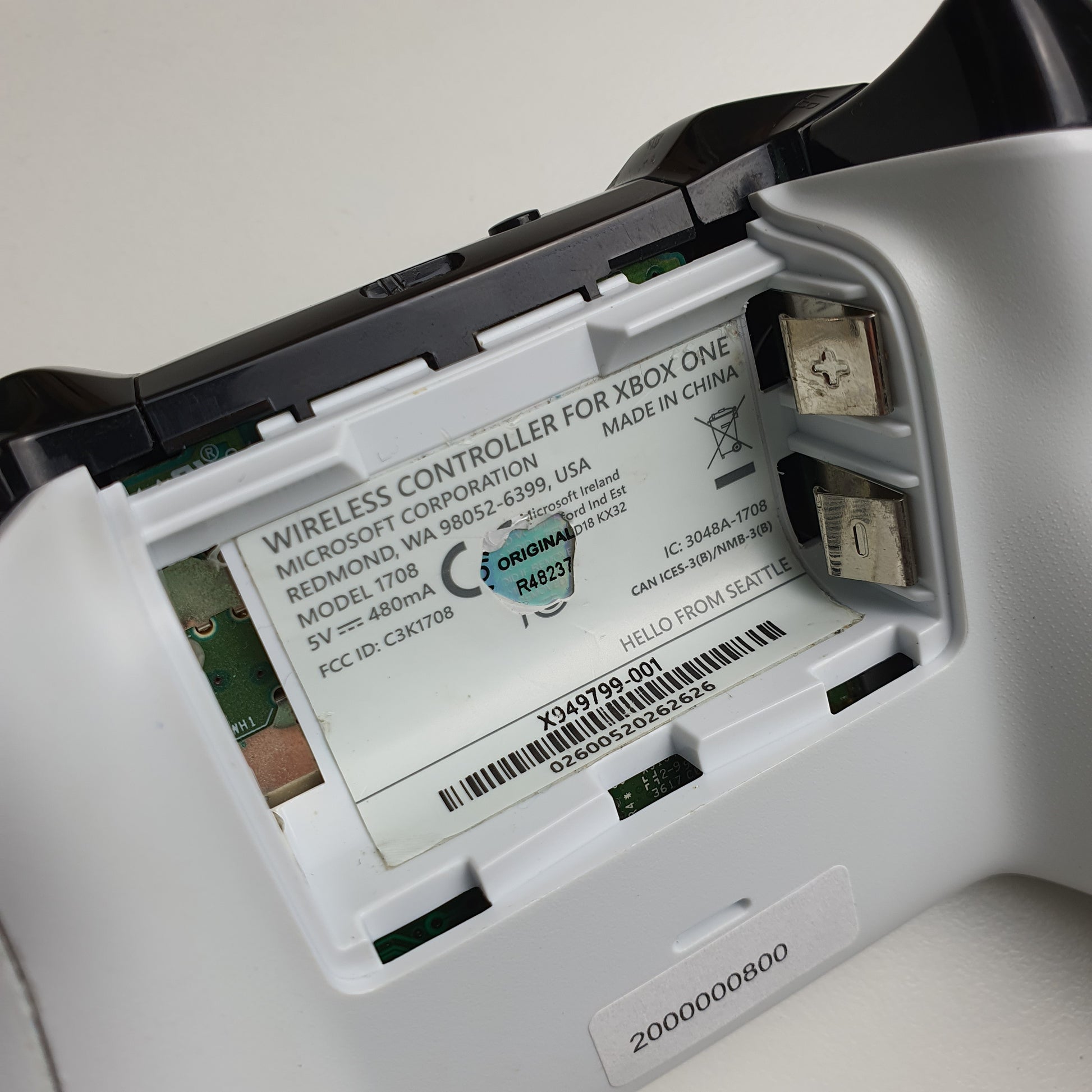 Close-up of a battery compartment on a white Xbox One controller on a light grey background
