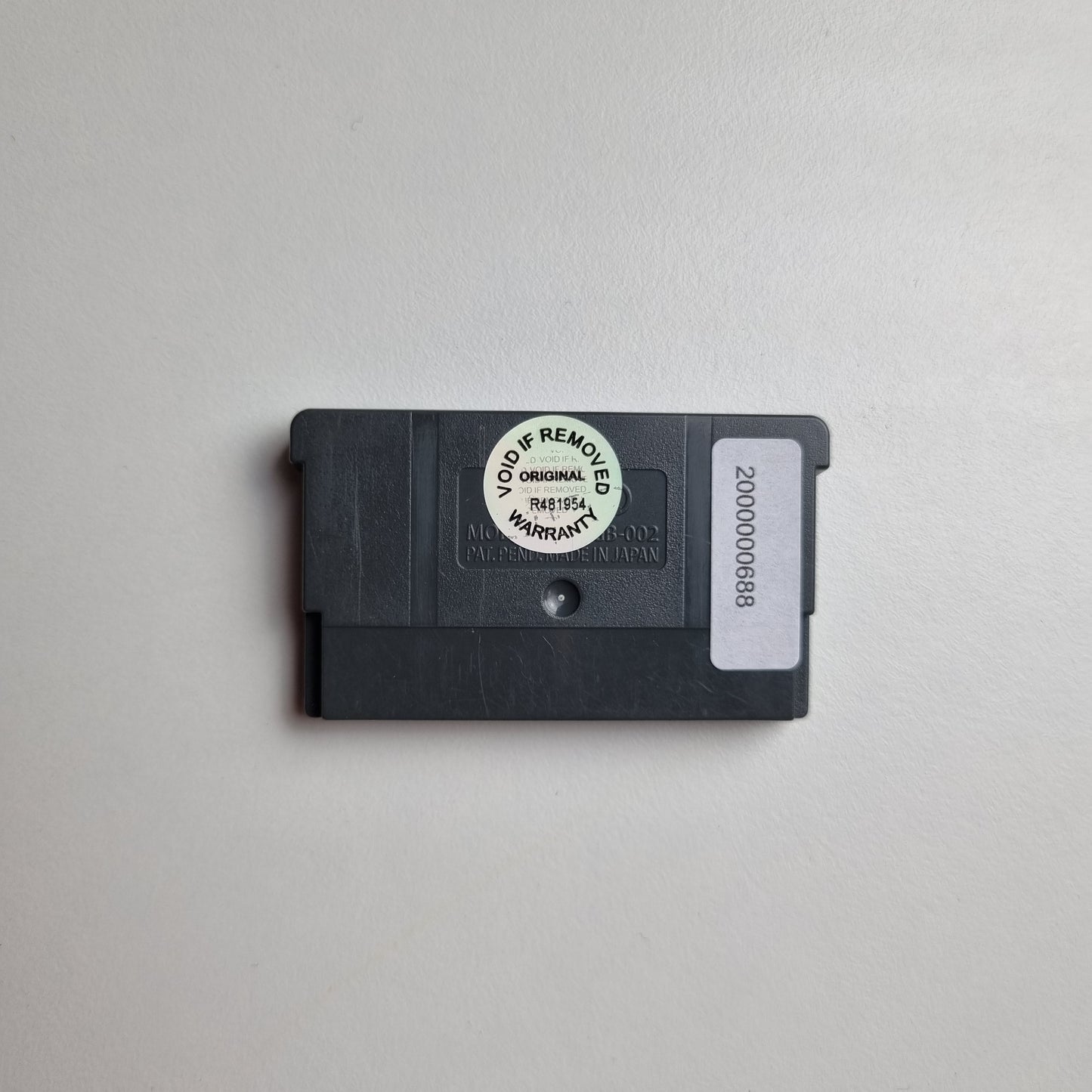 Back of a Nintendo Game Boy Advance cartridge showing an asset tag and void sticker, on a light grey background