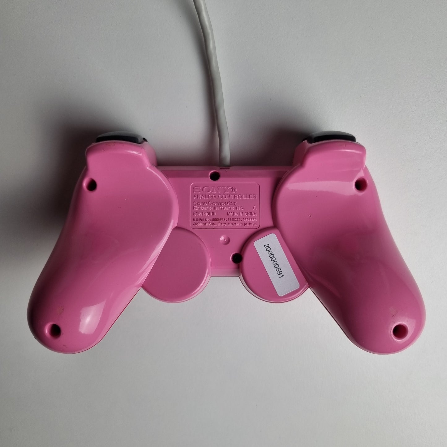 Underside of an official Sony PlayStation 2 DualShock refurbished pink wired controller on a light gray background