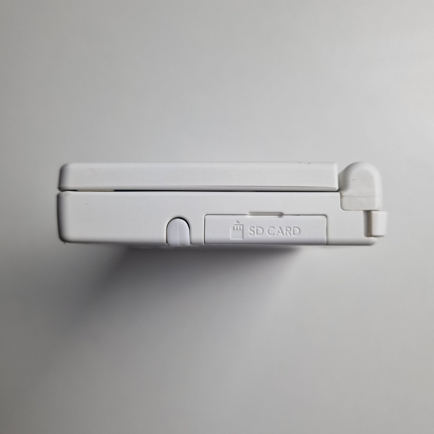 Side of a white Nintendo DSi handheld console on a light grey background.