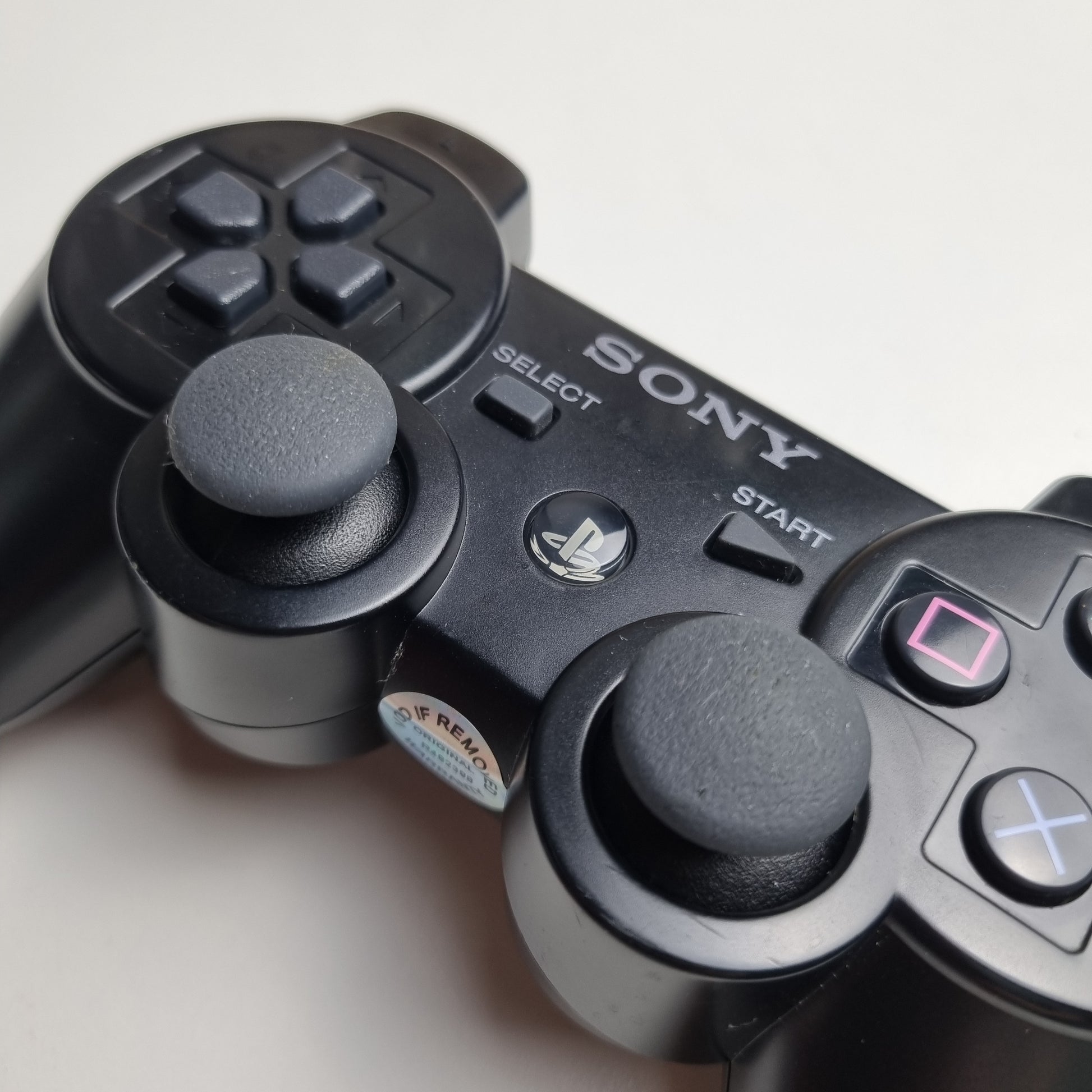 Close-up of a official Sony PlayStation PS3 SIXAXIS black wireless controller on a white background.