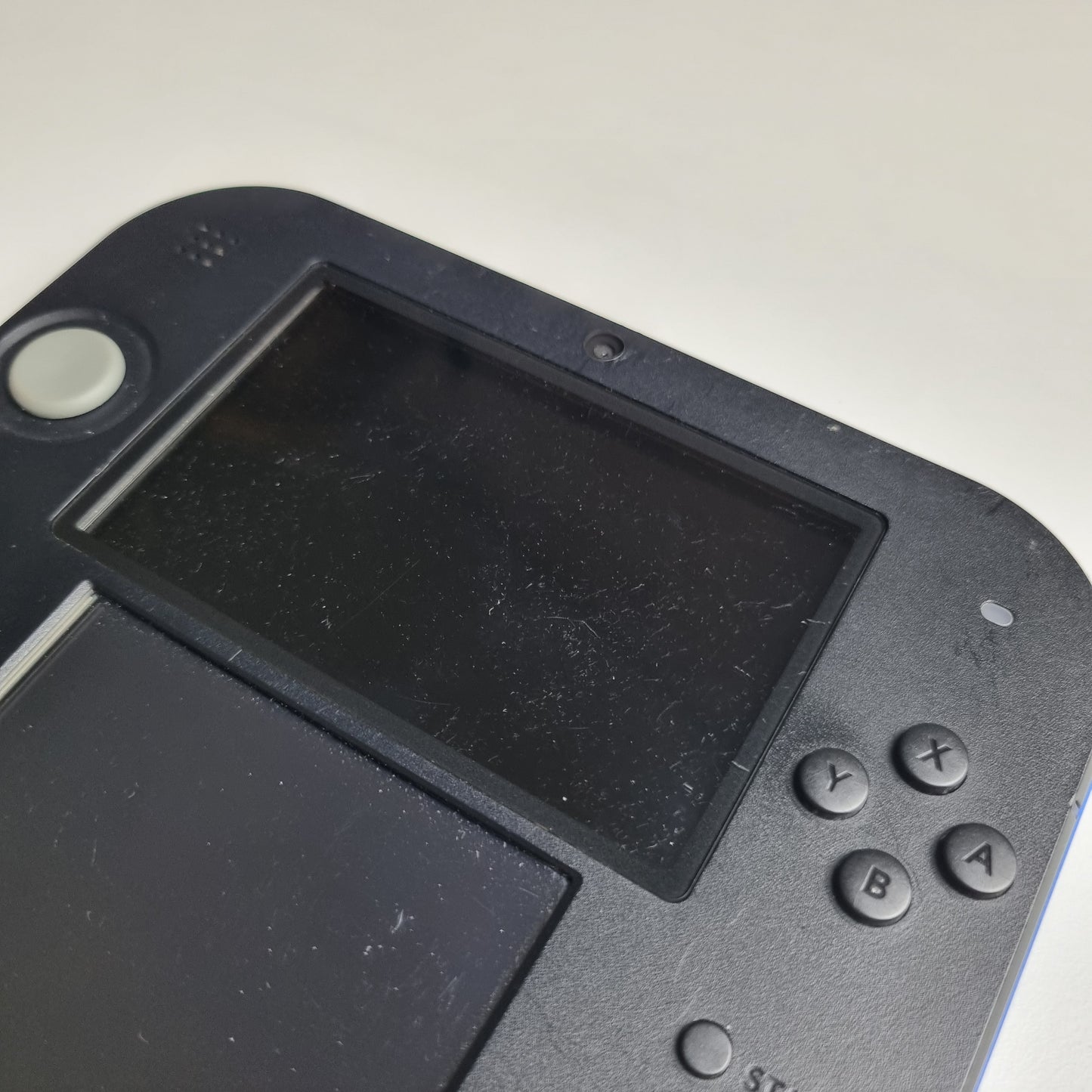 Close-up of a handheld gaming console showing surface scratches with a screen and control buttons on a light grey background