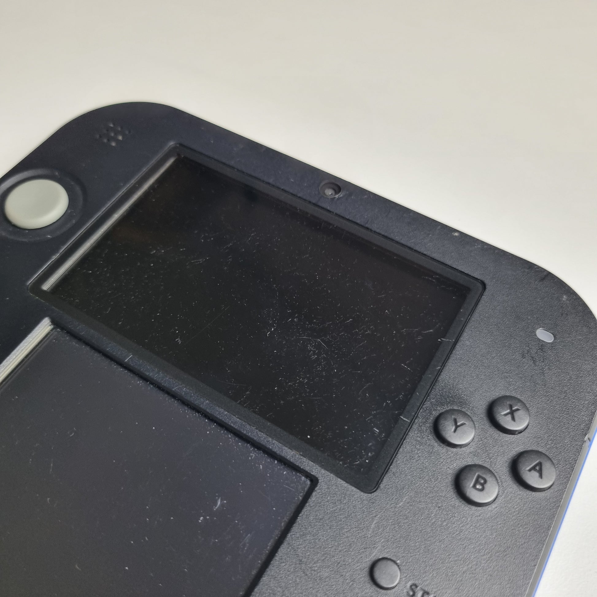 Close-up of a handheld gaming console showing surface scratches with a screen and control buttons on a light grey background