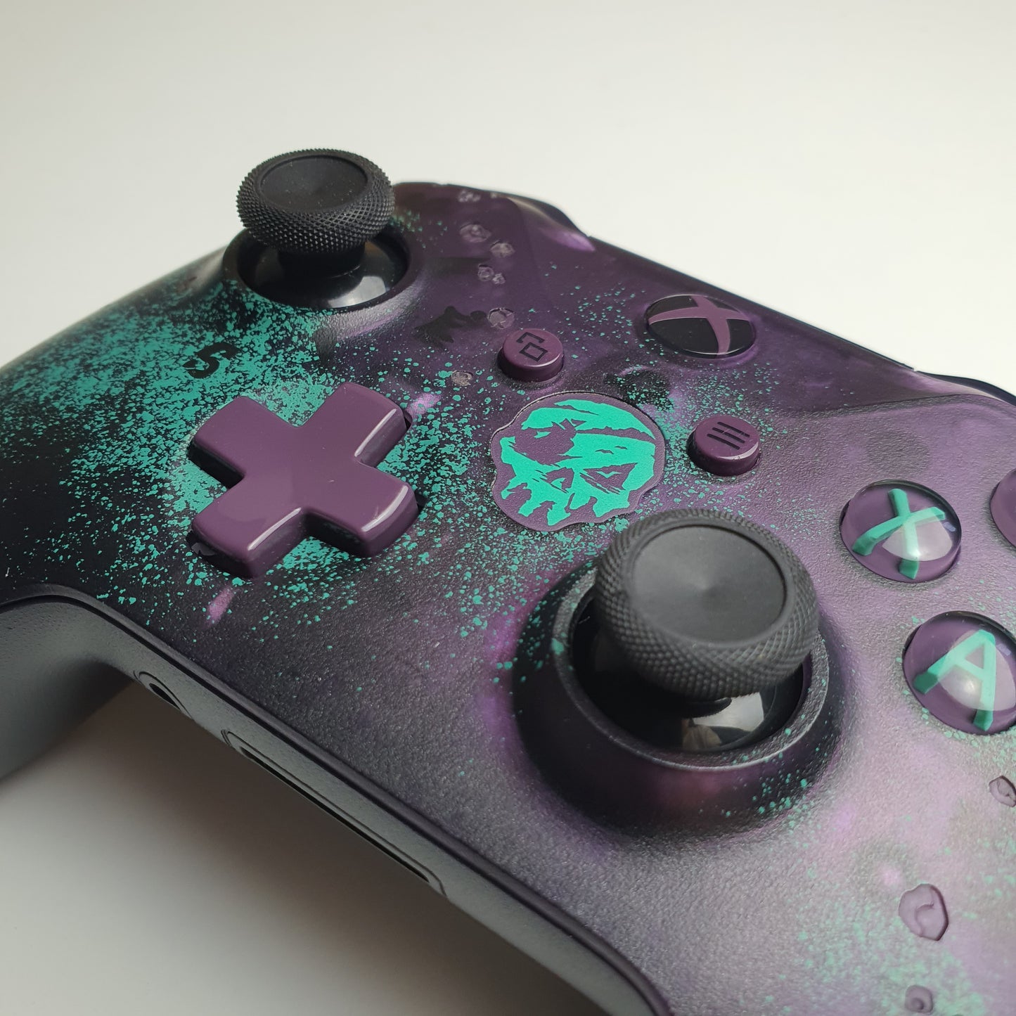 Close-up of a purple and teal Xbox One 'Sea of Thieves' controller with splatter design