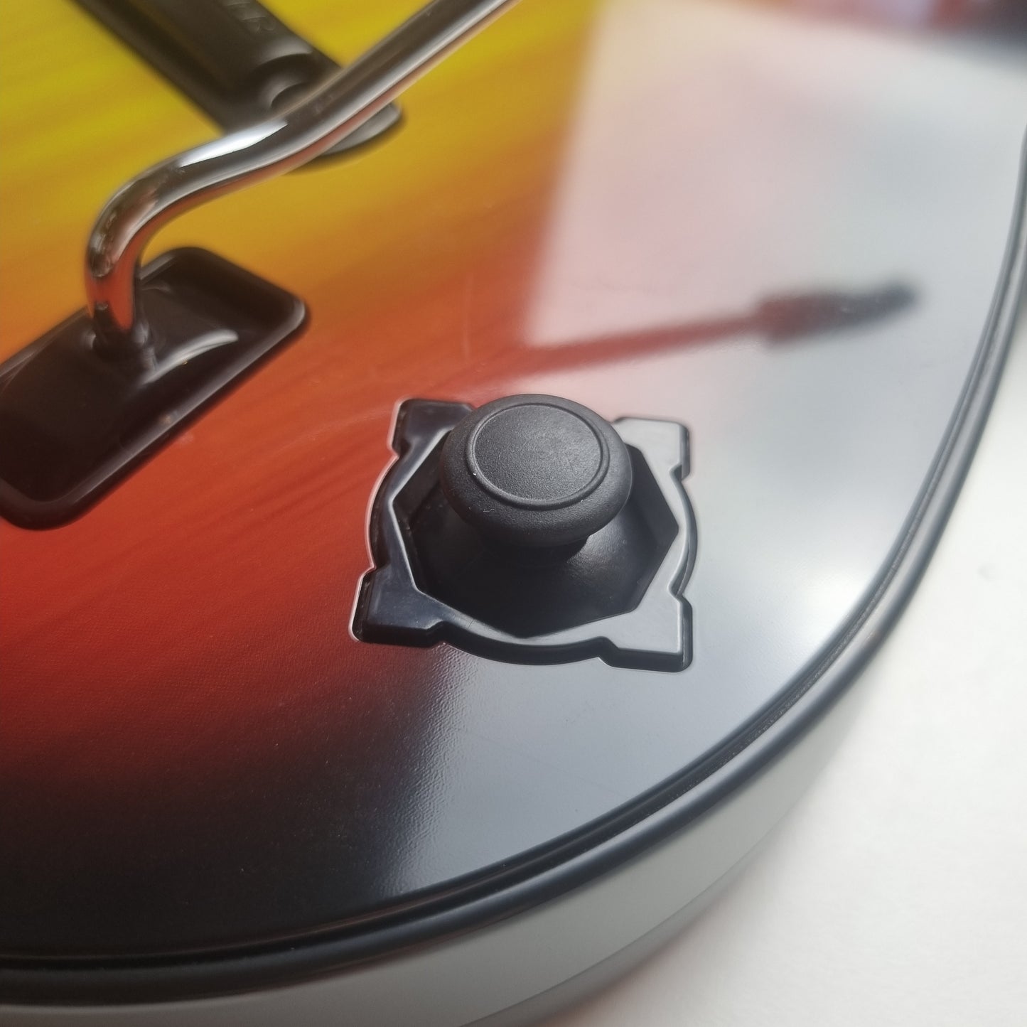 Close-up of the black analog stick of a official RedOctane Nintendo Wii sunburst guitar controller on a white background.