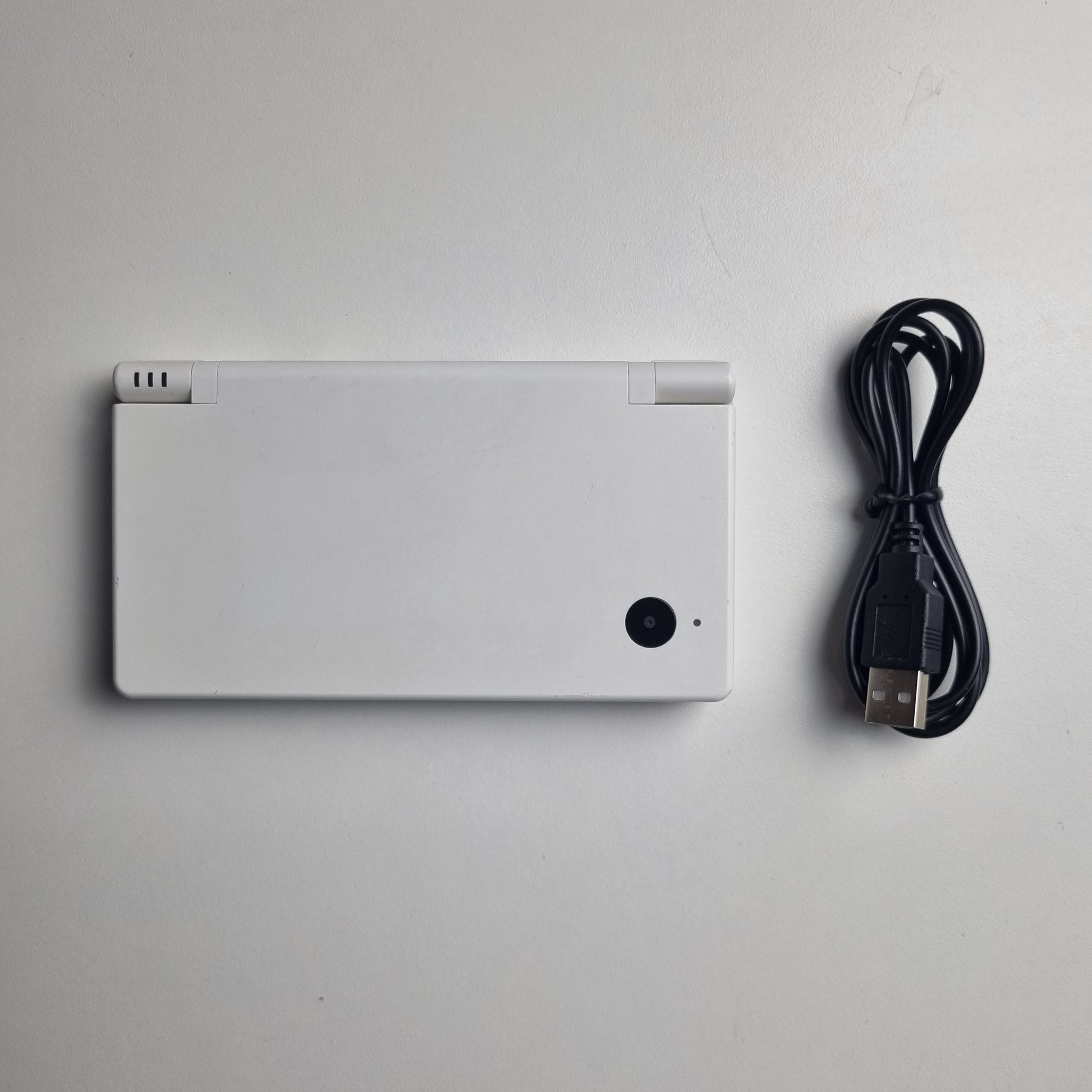 White Nintendo DSi handheld console with a black USB charging cable on a light grey background.