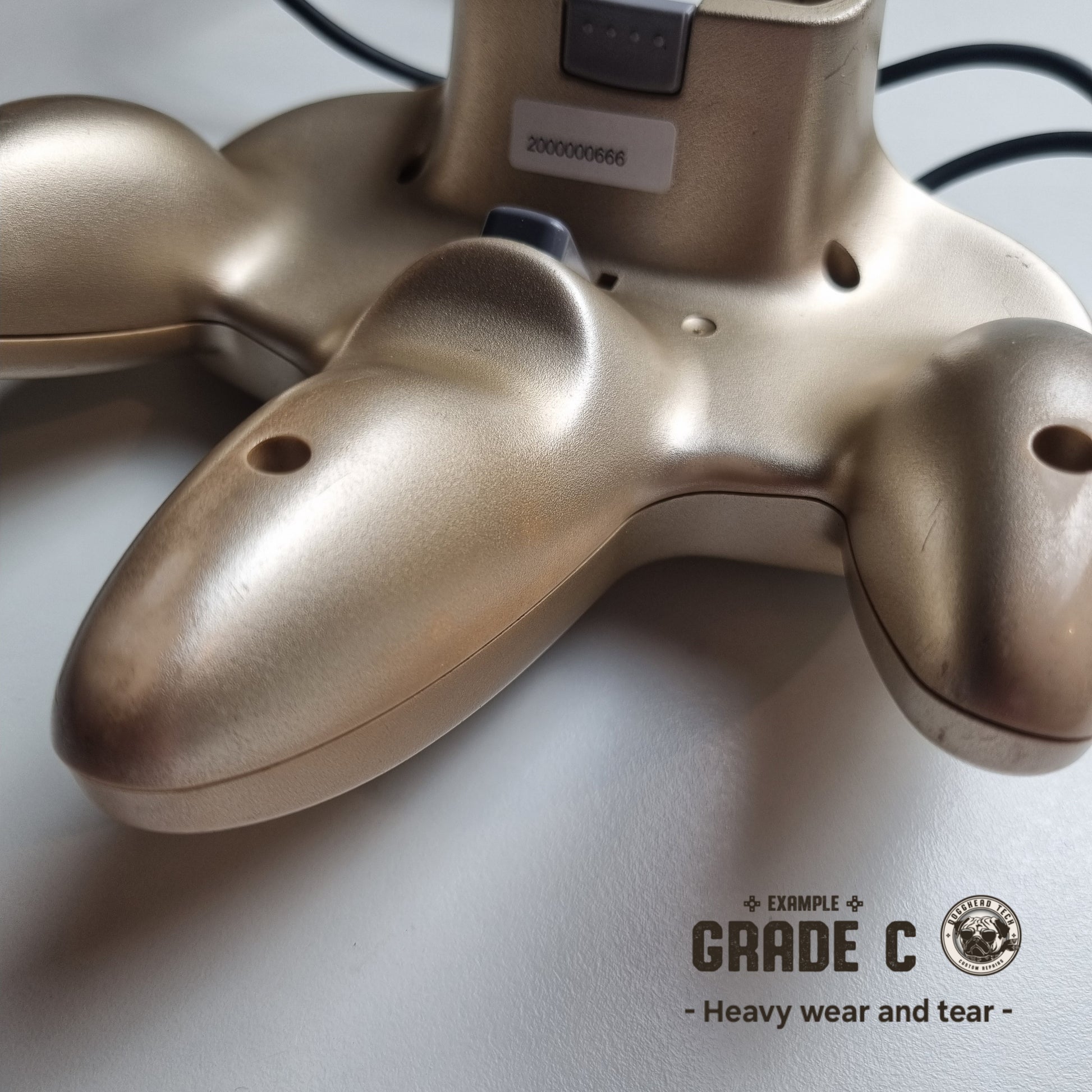 Close-up of the back part of a refurbished modified gold Nintendo 64 controller, showing significant wear and tear. The text reads 'Example Grade C: Heavy wear and tear'.