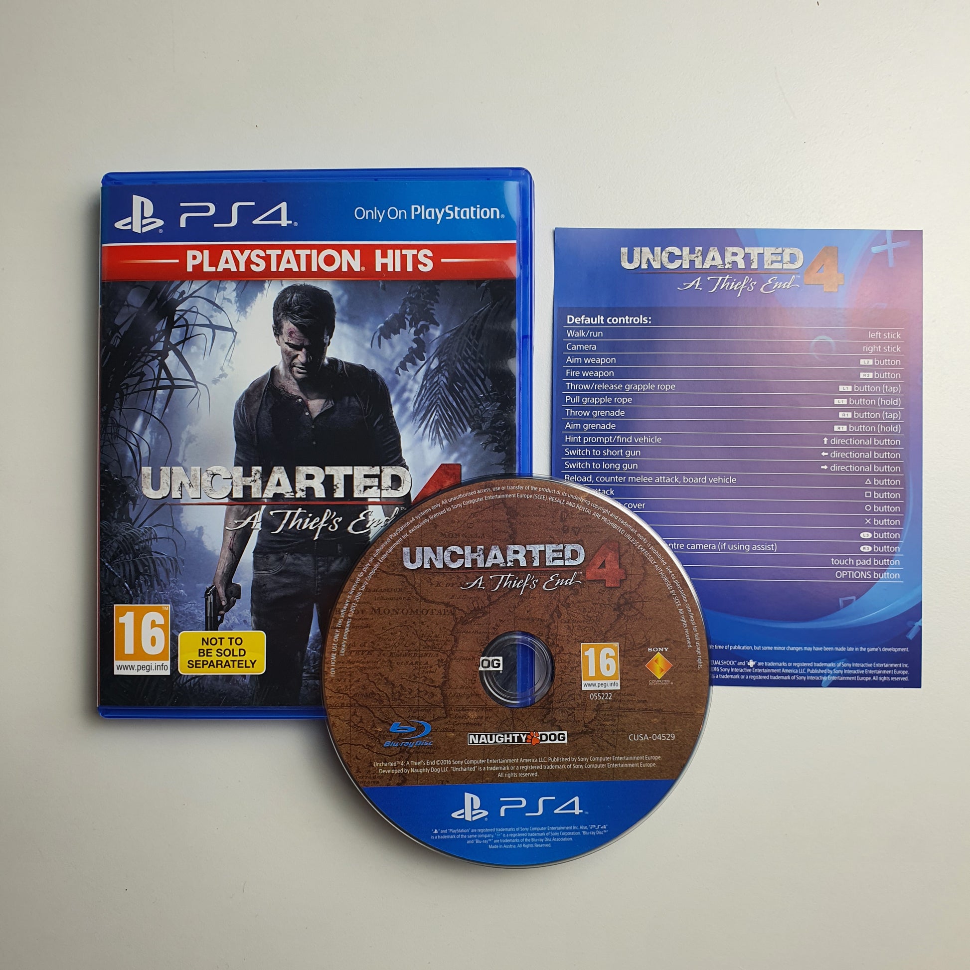 Game disc, case and inserts of 'Uncharted 4' for PlayStation 4 on a light grey background