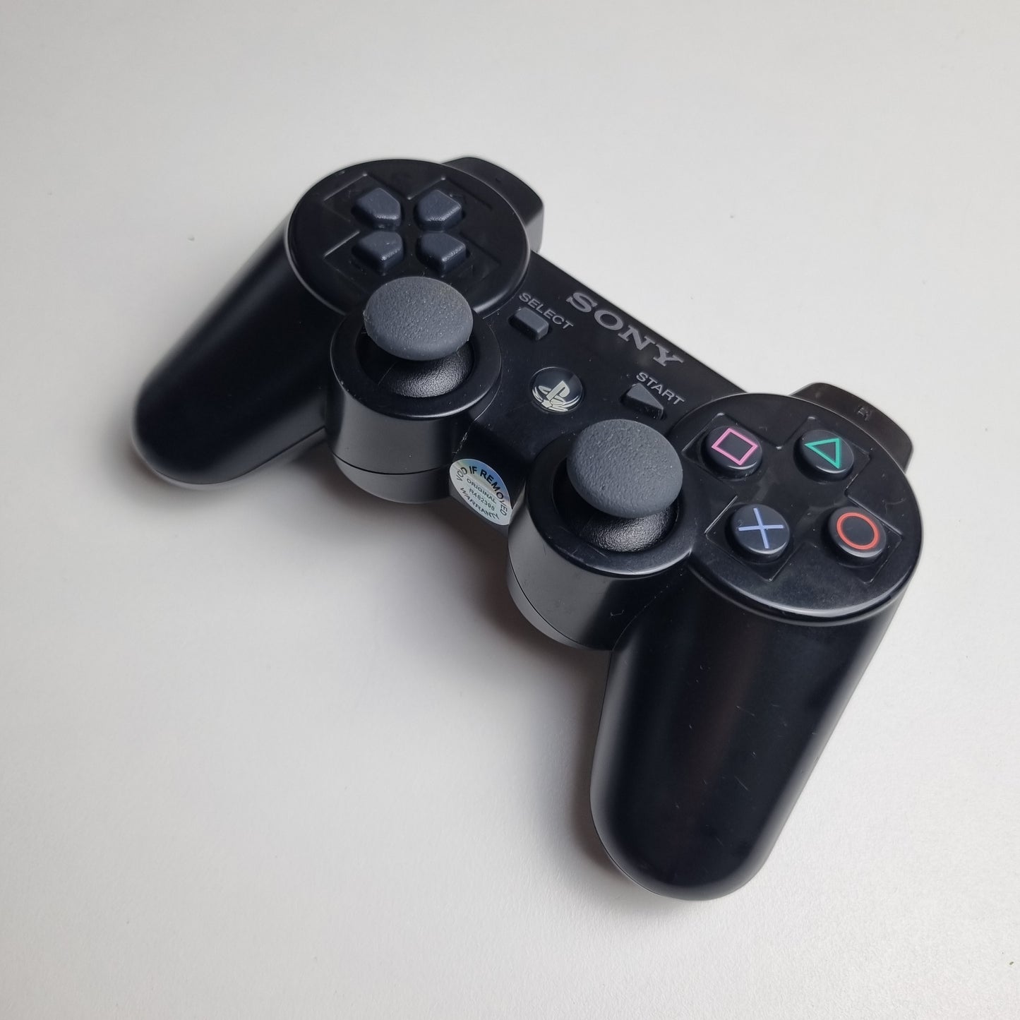 Angled picture of a official Sony PlayStation PS3 SIXAXIS black wireless controller on a white background.