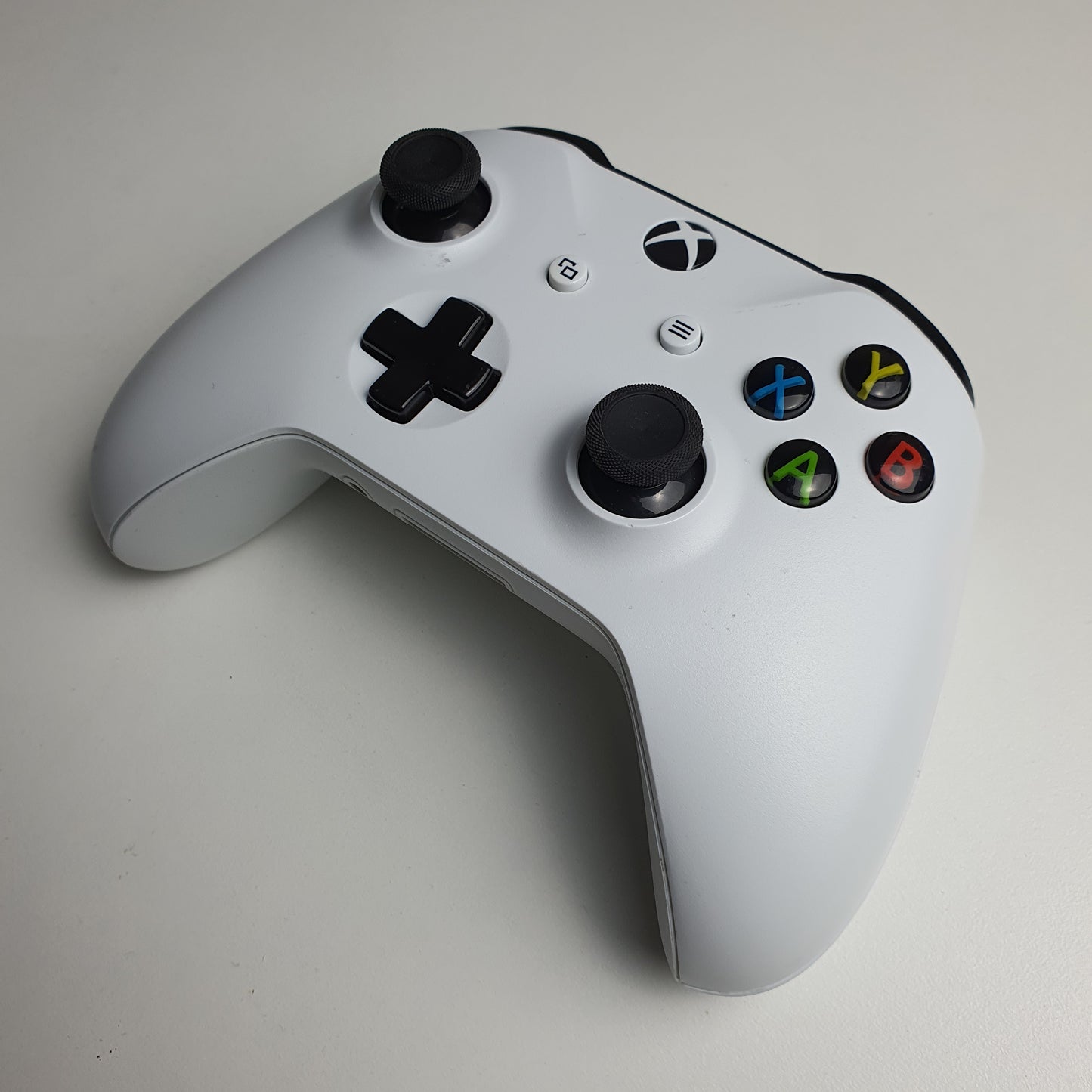 A white Xbox One controller with black buttons on a light grey background