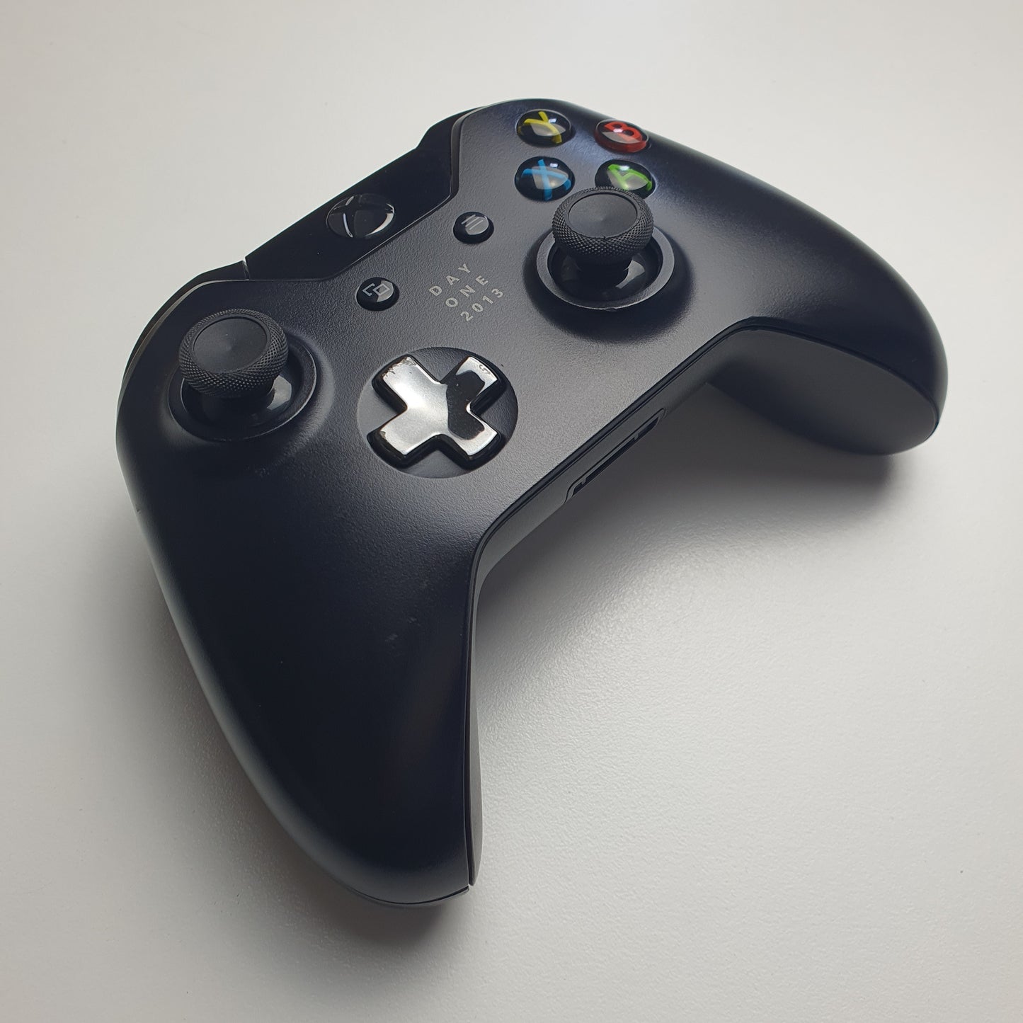 Front of a black 'Day One 2013' Xbox One controller on a white background