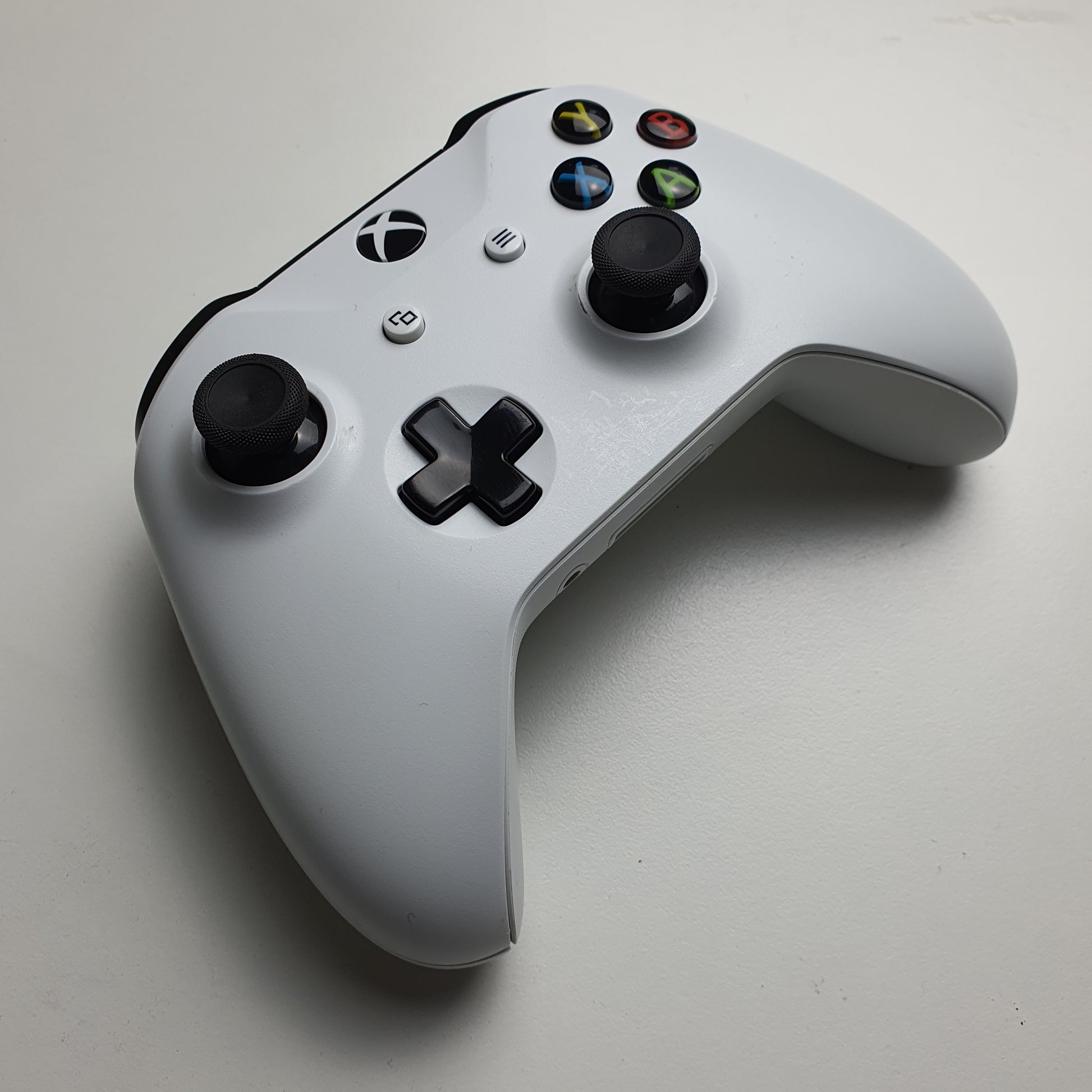 A white Xbox One controller with black buttons on a light grey background
